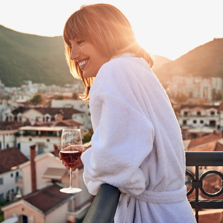 Young woman having a glass of wine on a balcony with a view. 