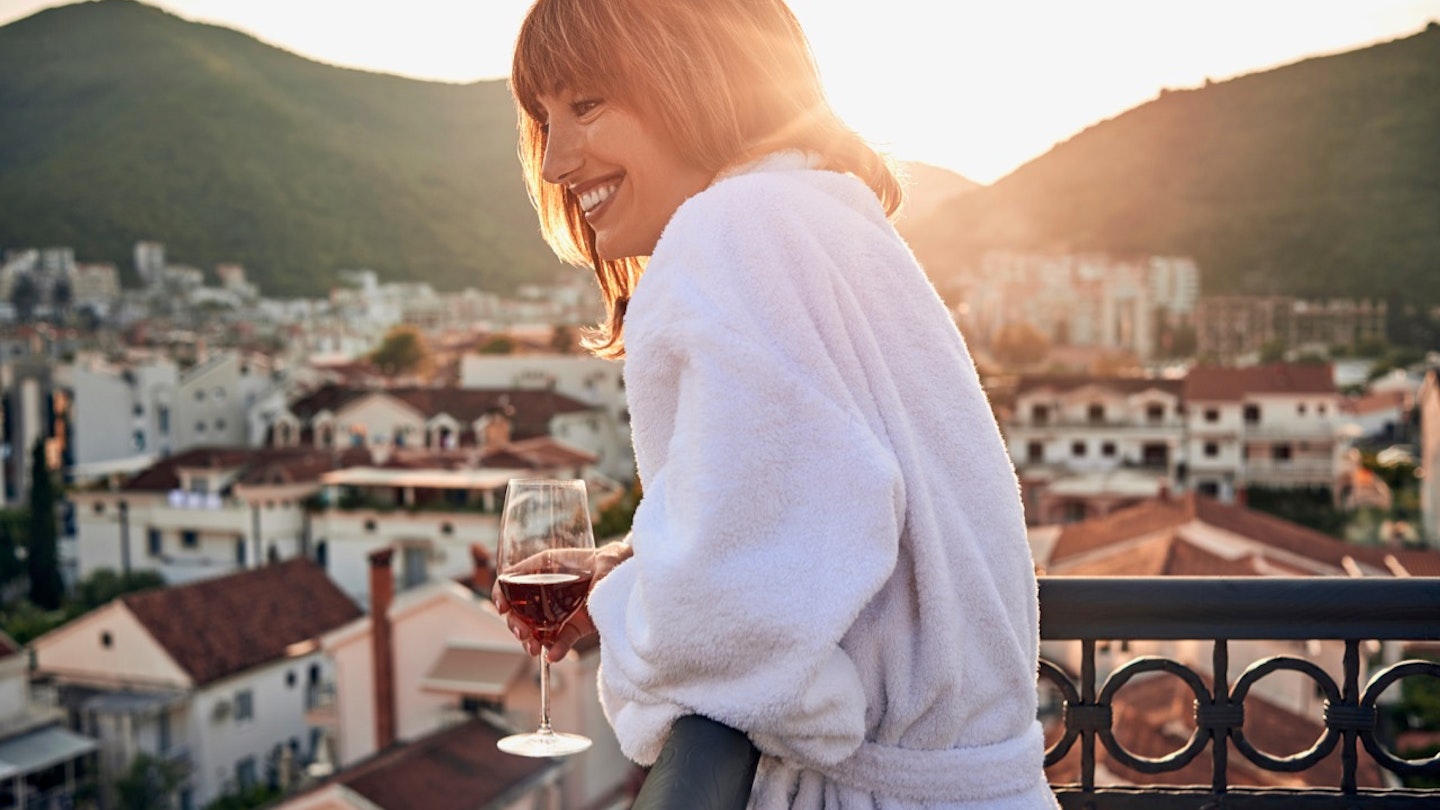 Young woman having a glass of wine on a balcony with a view. 