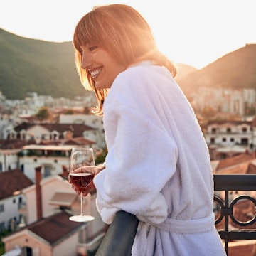Young woman having a glass of wine on a balcony with a view.