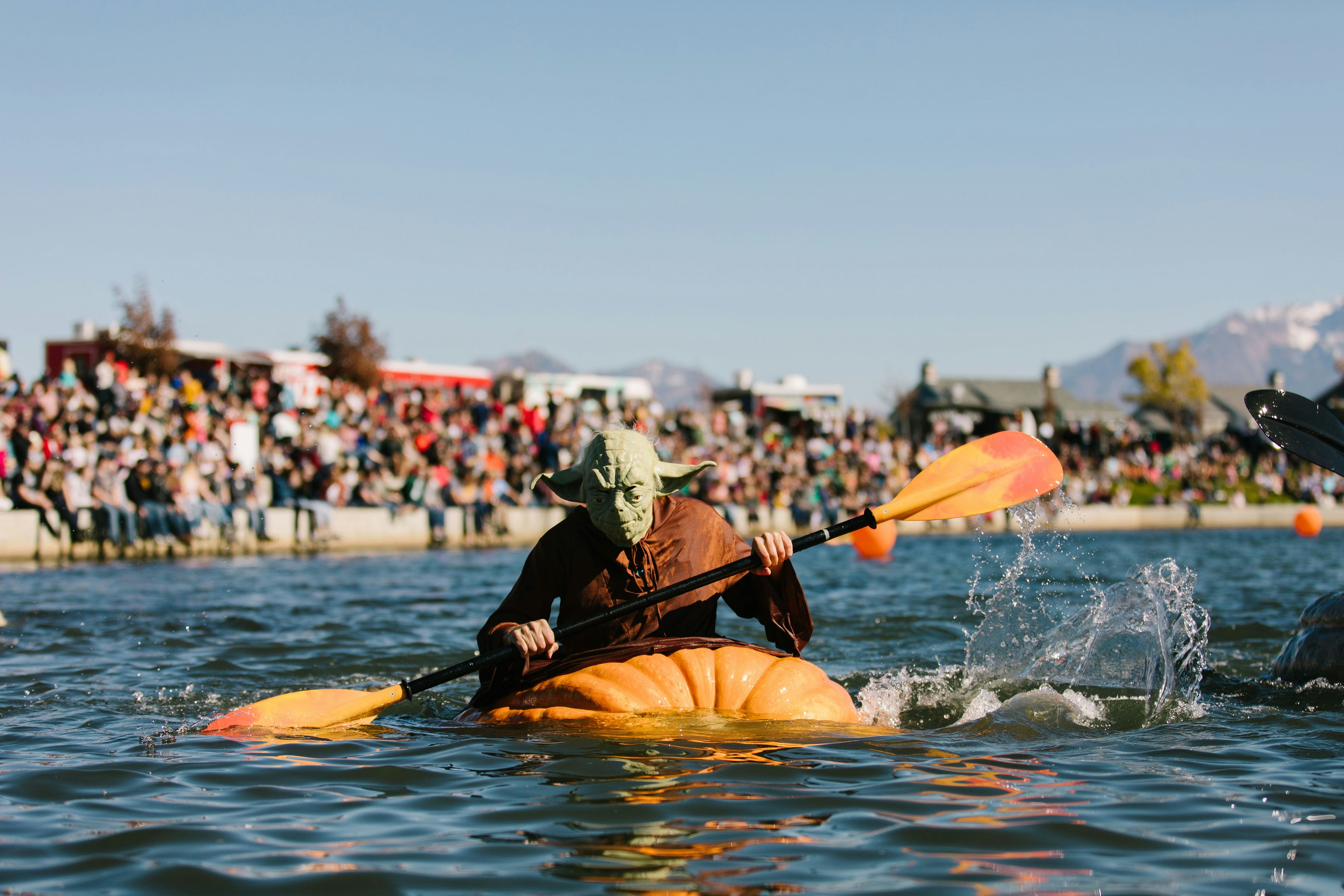 A person dressed as Star Wars character Yoda, paddles through the water in a large pumpkin