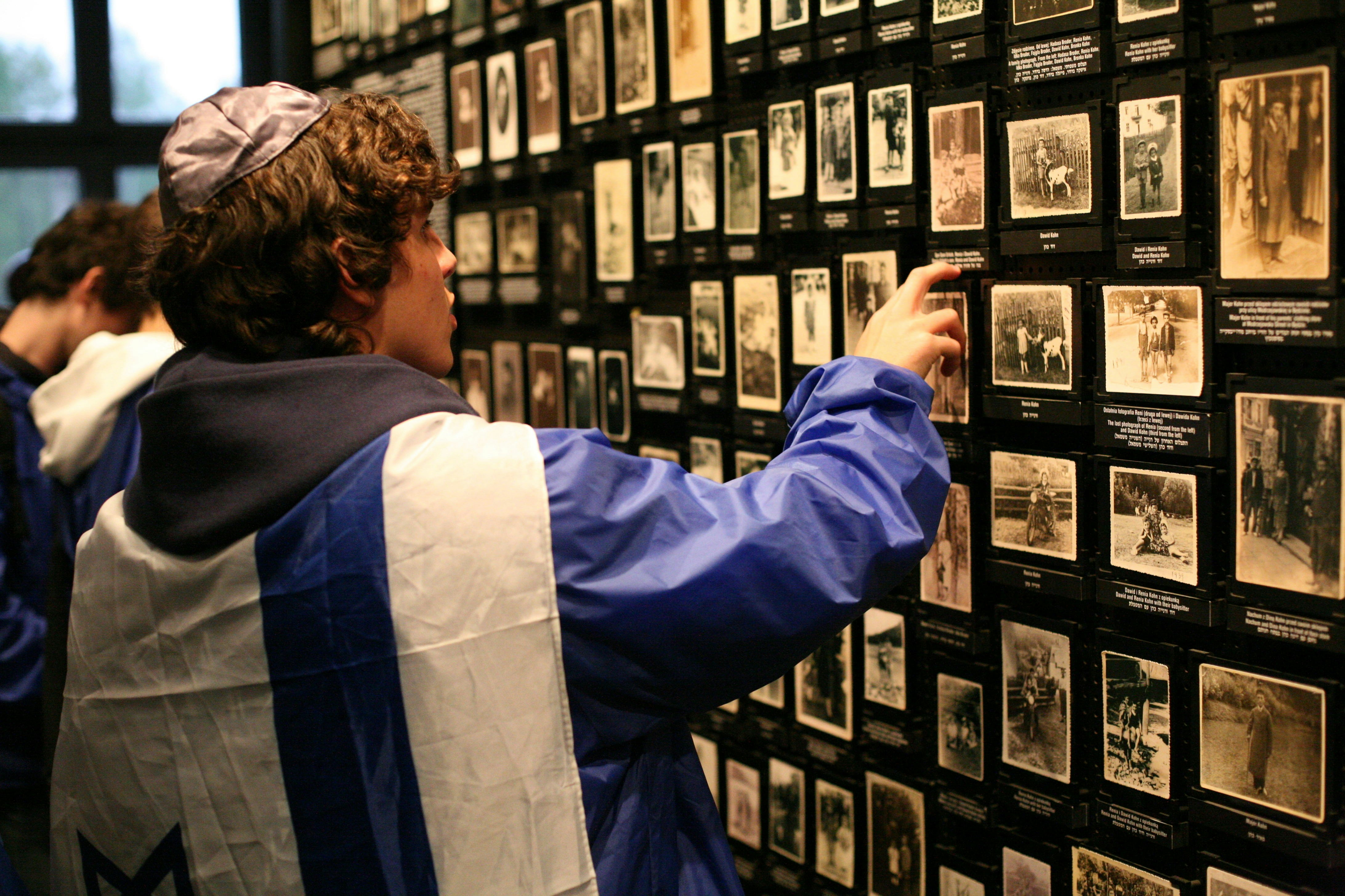A young man wearing a yamaka hat looks at photos in the holocaust museum