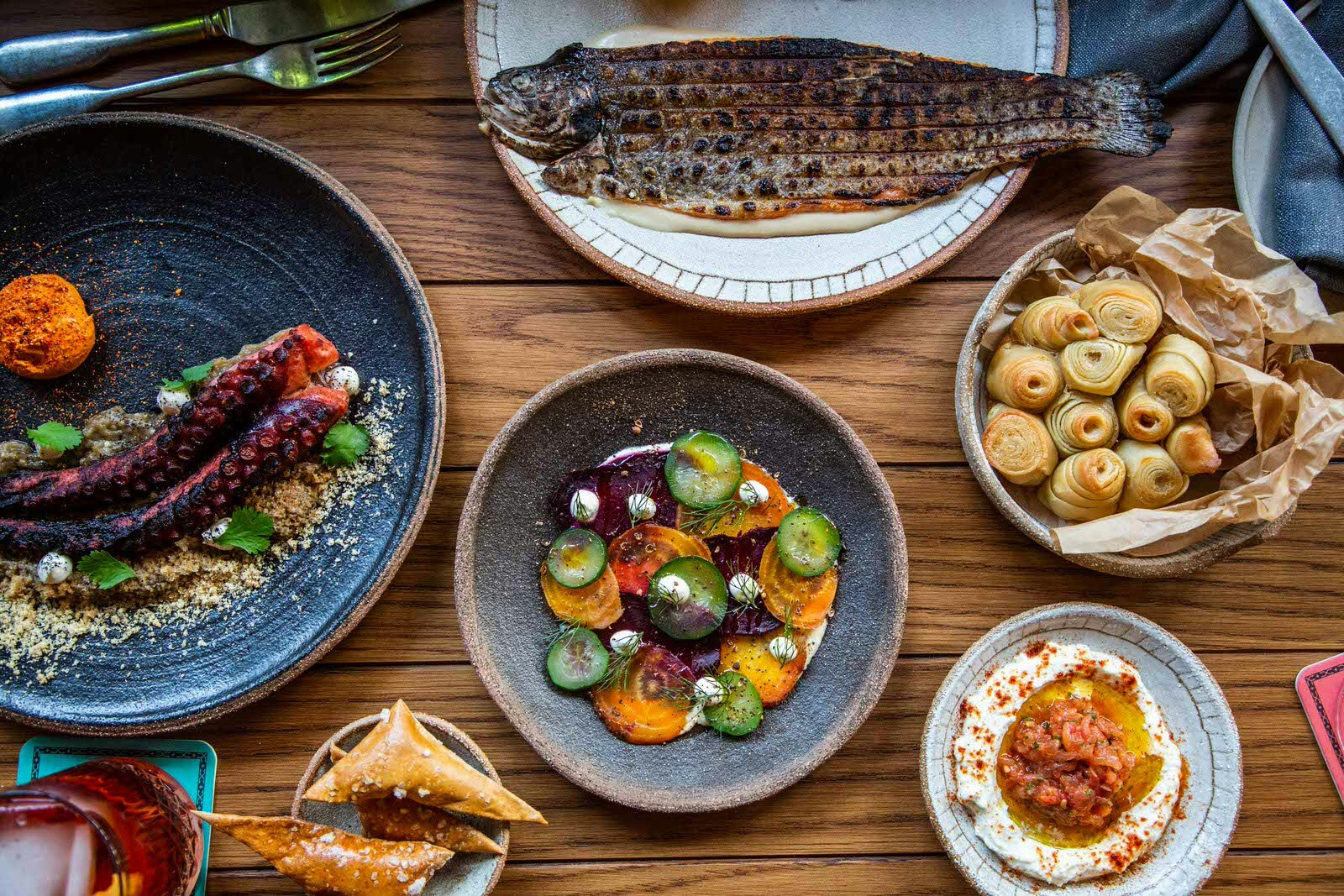 Lots of small dishes laid on a wooden table including grilled fish, octopus, hummus and pastries at Za Za Ta in Brisbane.