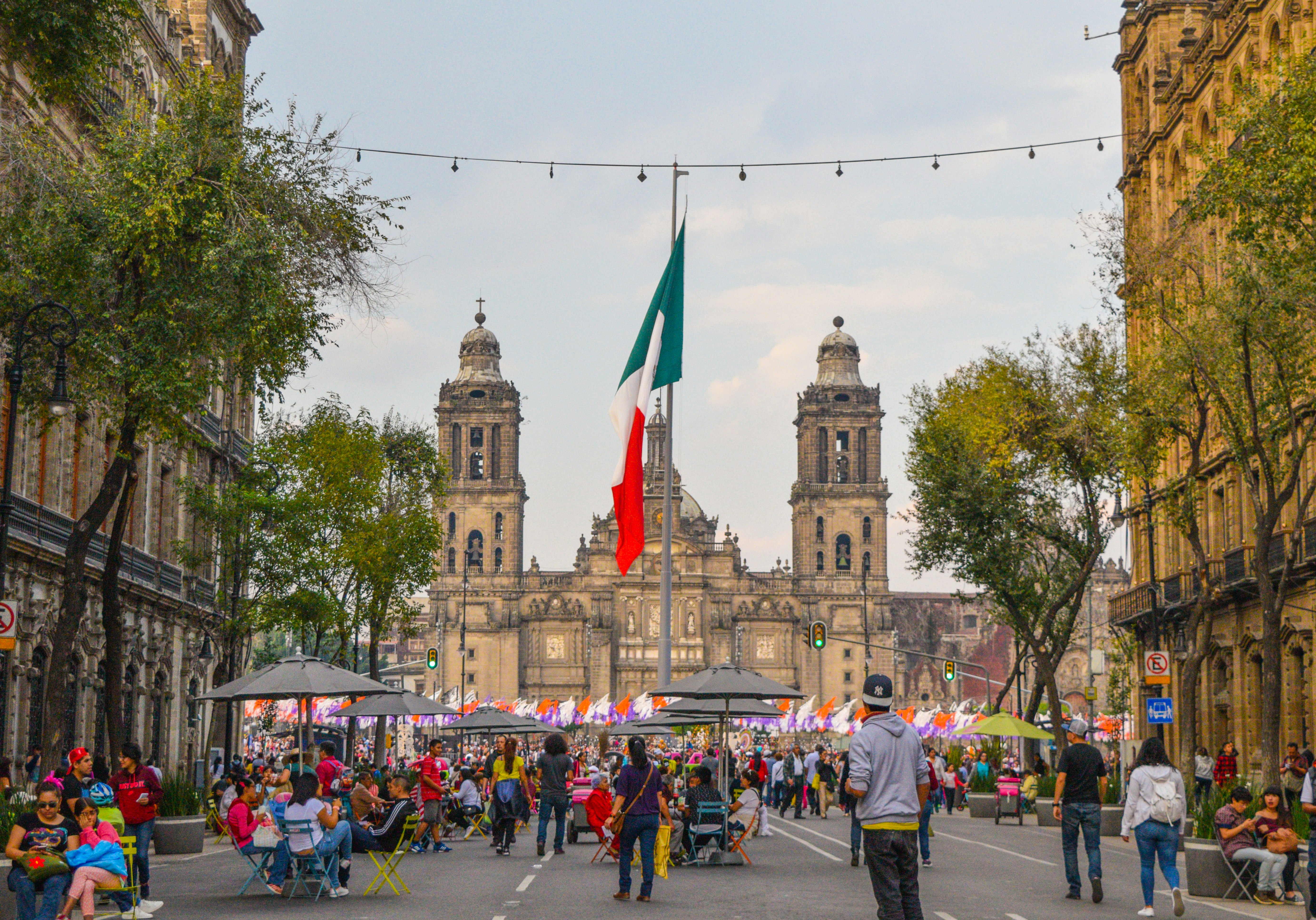 The National Cathedral in Mexico City with a large Mexican flag and a variety of people gathering in frong