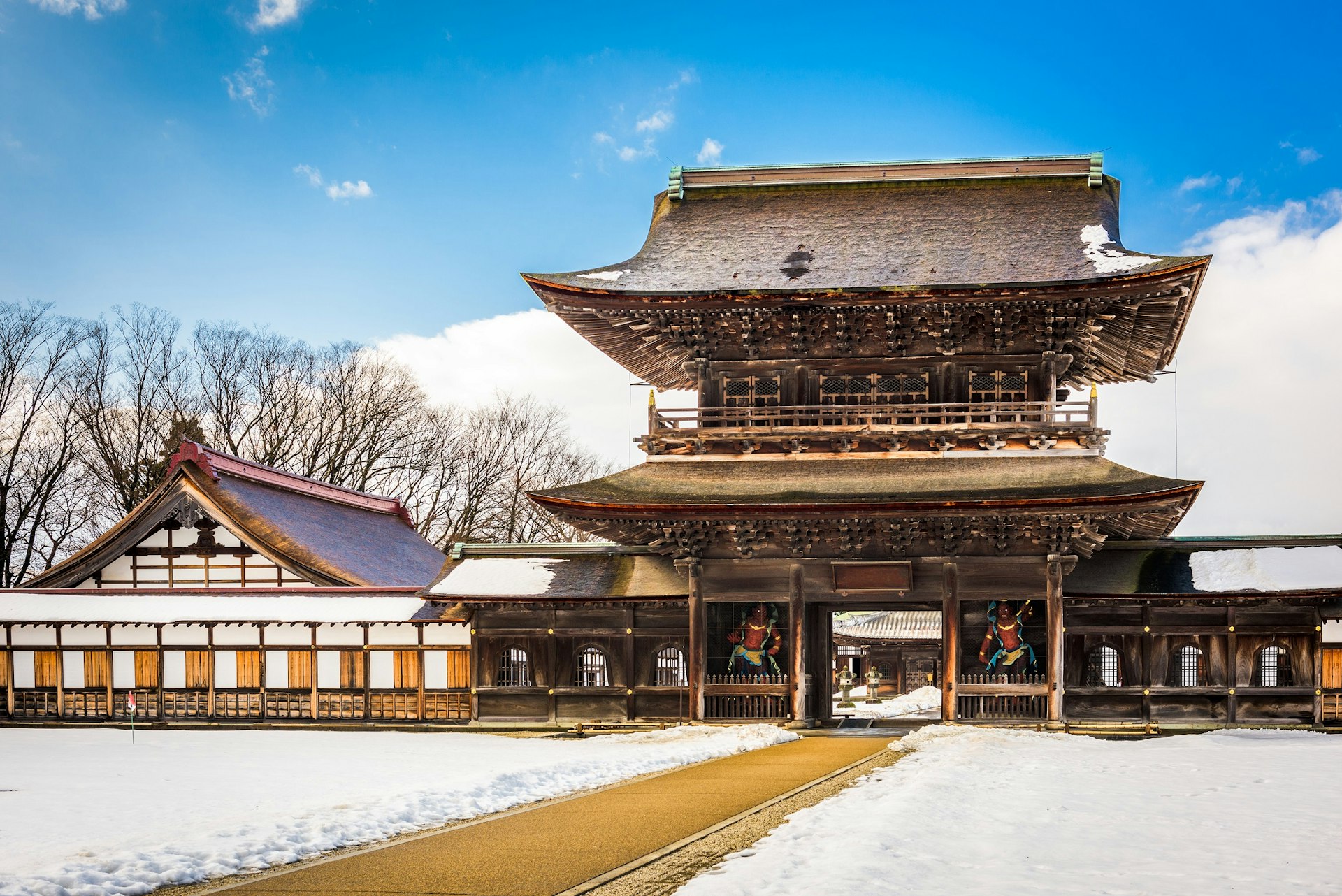A tall and large wooden temple, with a traditional Japanese slanting roof. The ground around the temple is covered in snow.