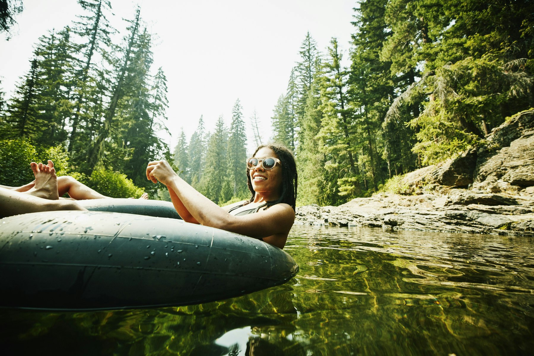 A smiling woman with sunglasses floating down a river on an inner tube on a sunny day.