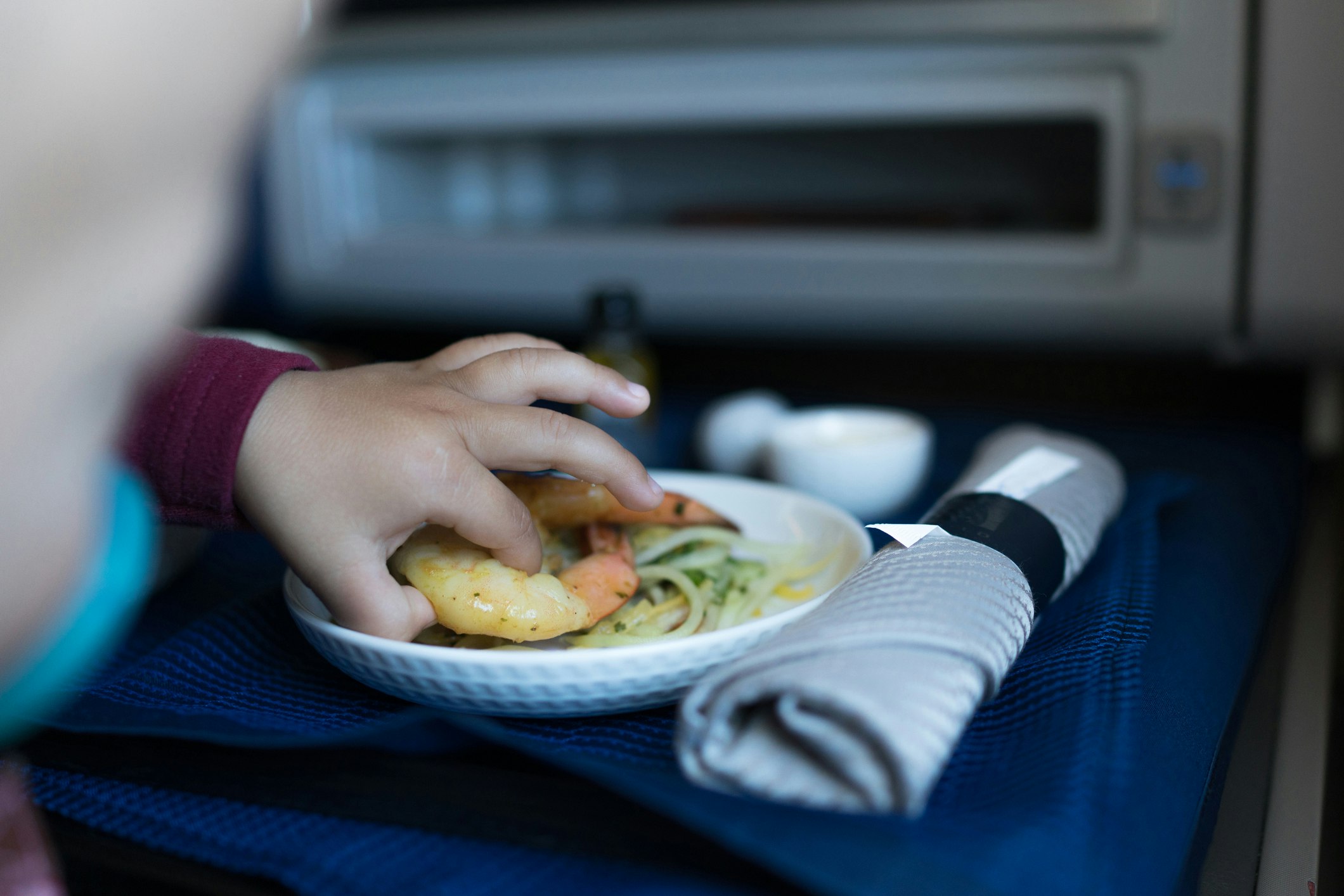A child eats a shrimp from a airplane tray. 