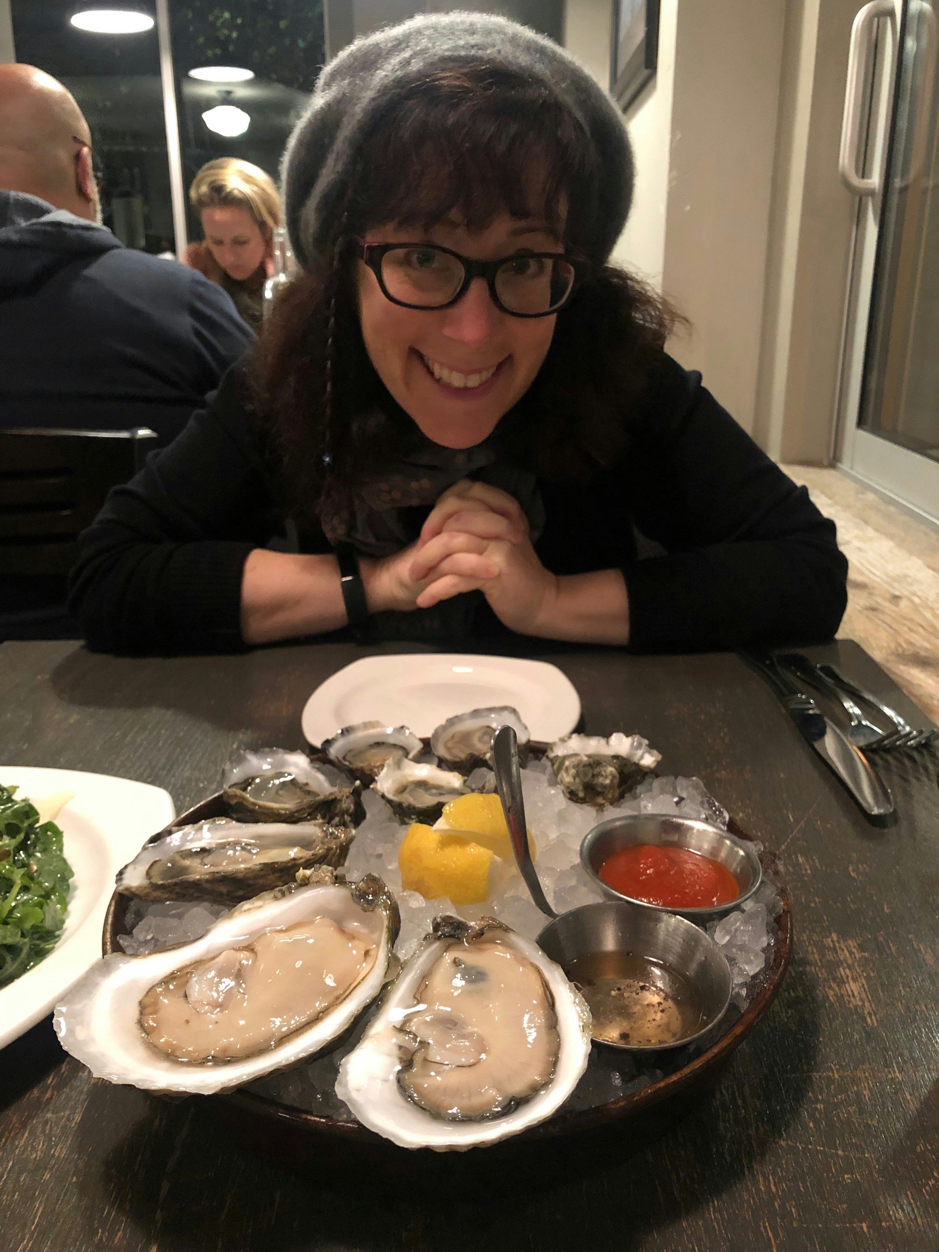 A woman smiling next to a plate of raw oysters