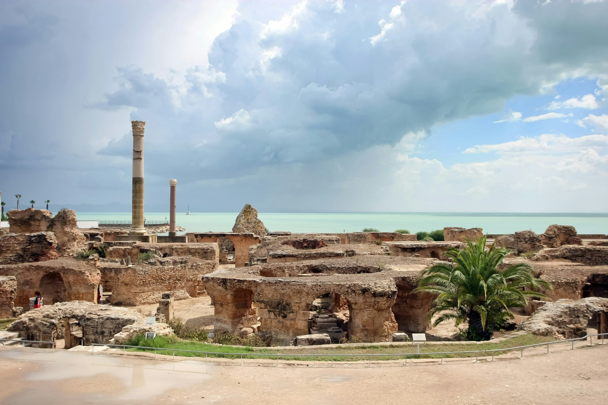 The image looks across a series of thick stone arches and two stone columns towards the sea, which has a thick thunder cloud over it.