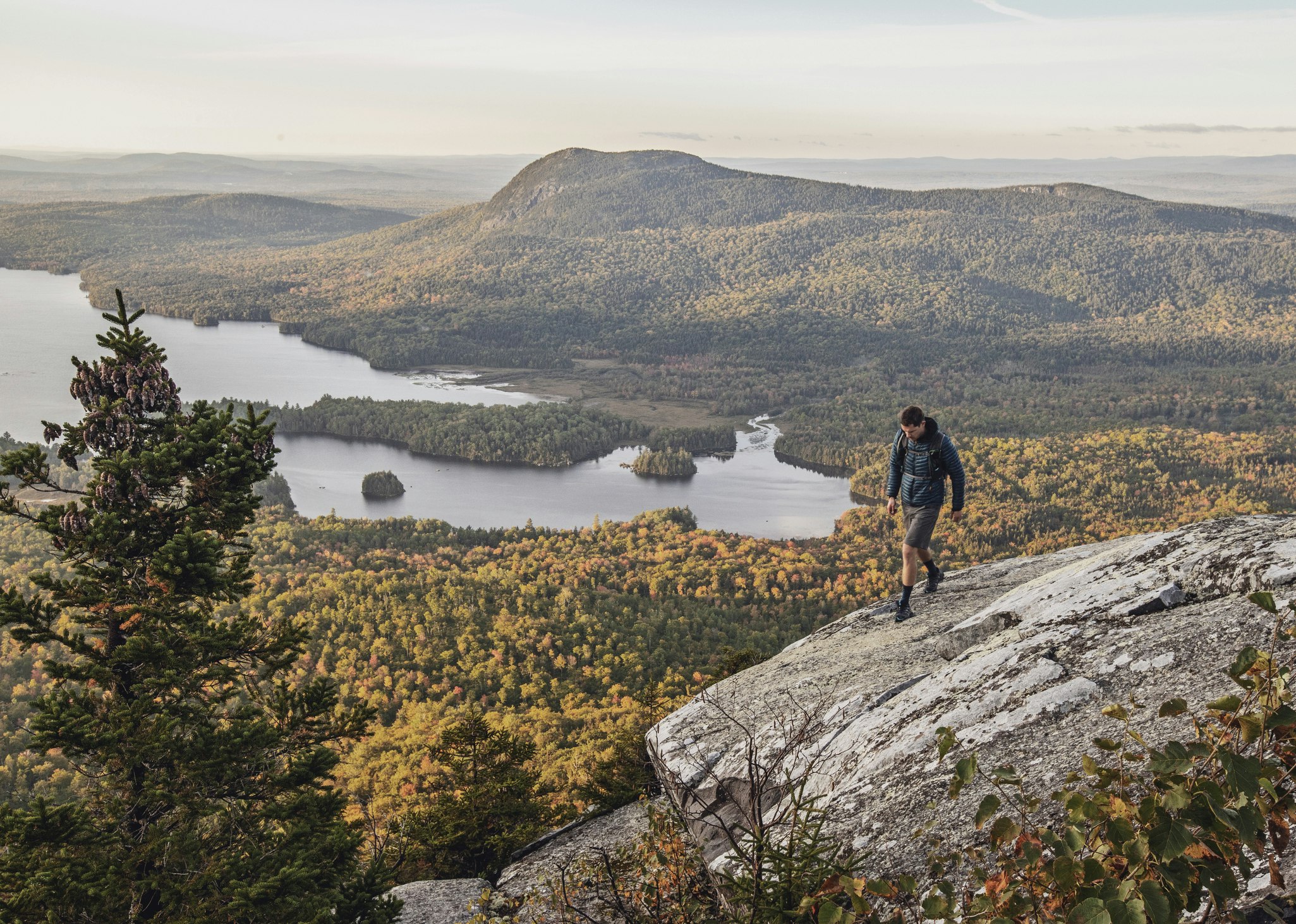 A man in hiking gear traverses a stony grey cliff in Maine along the Appalachian Trail