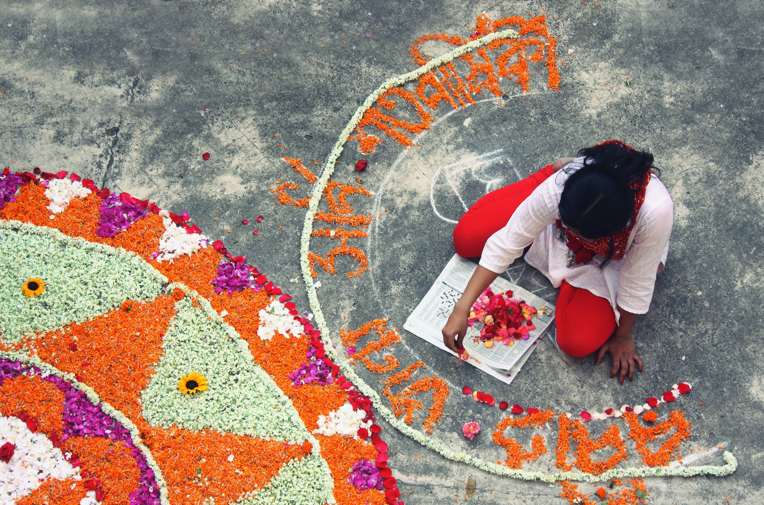 A woman sits on the ground making colourful patterns on the concrete using flower petals.