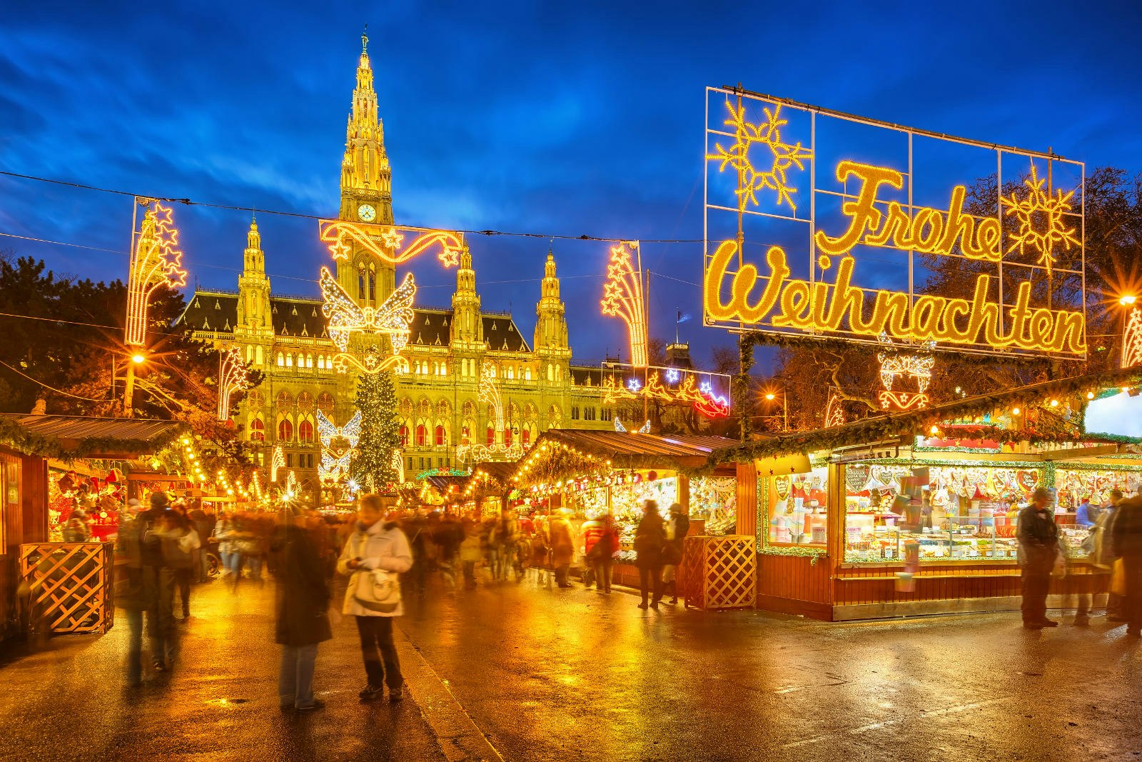 An illuminated Christmas market with a sign of lights spelling out Frohe Weihnachten, which means Merry Christmas in German