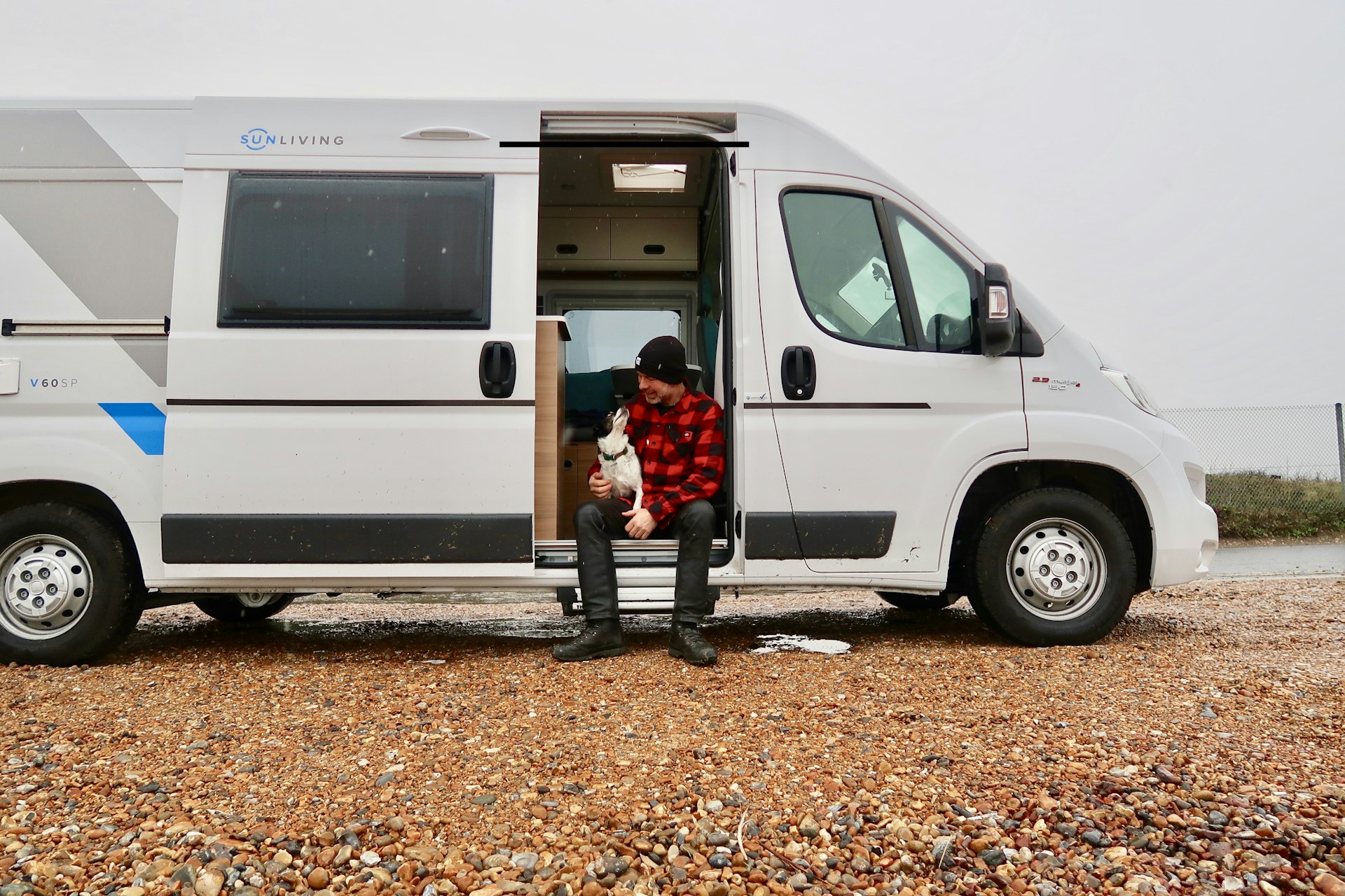 Author Andrew Ditton sits on the side of his van with his black and white dog. The white van is parked in a rural location.