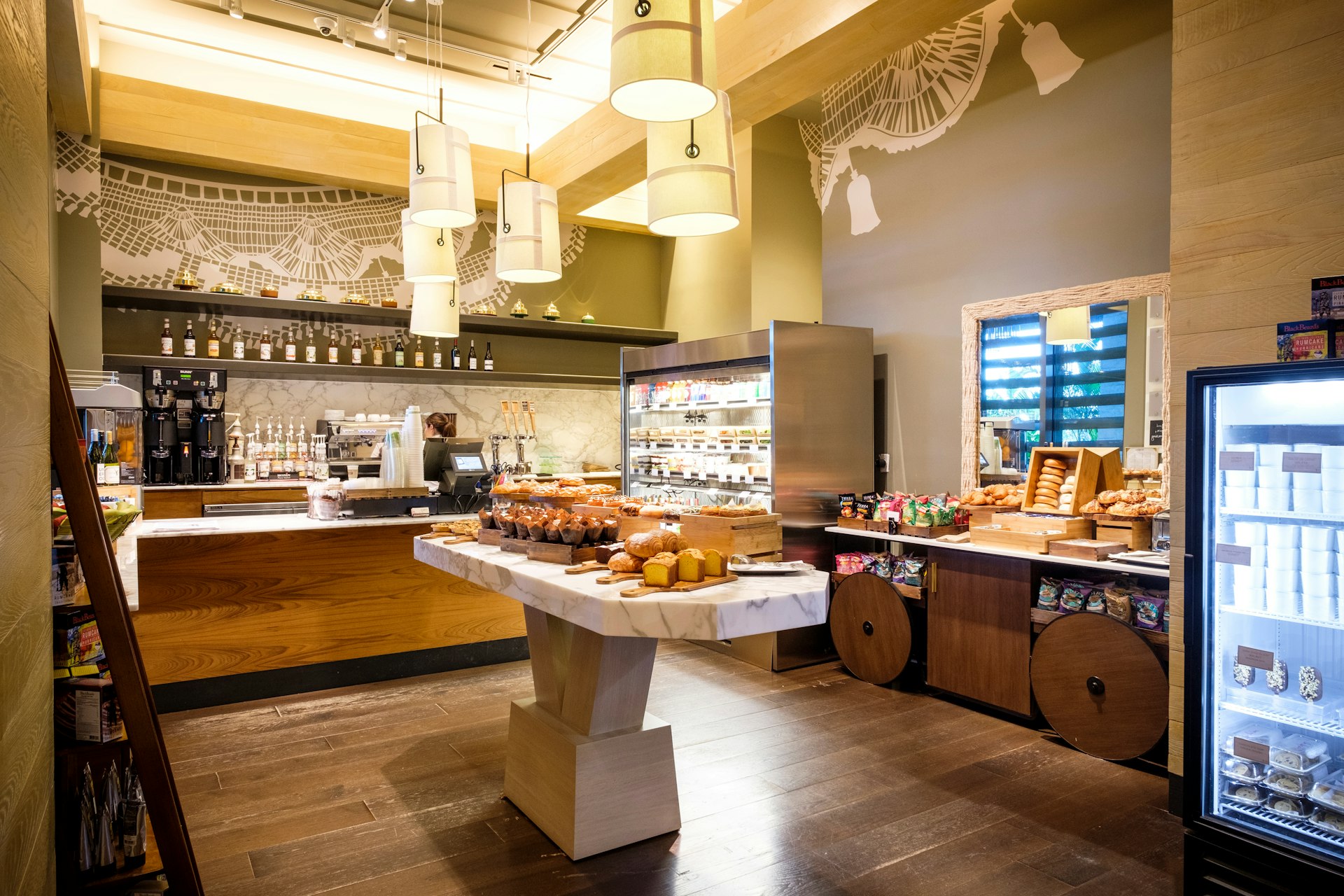 The interior of a restaurant; at the rear is a well-stocked bar area, while in the middle is a marble island station with bread and cakes.