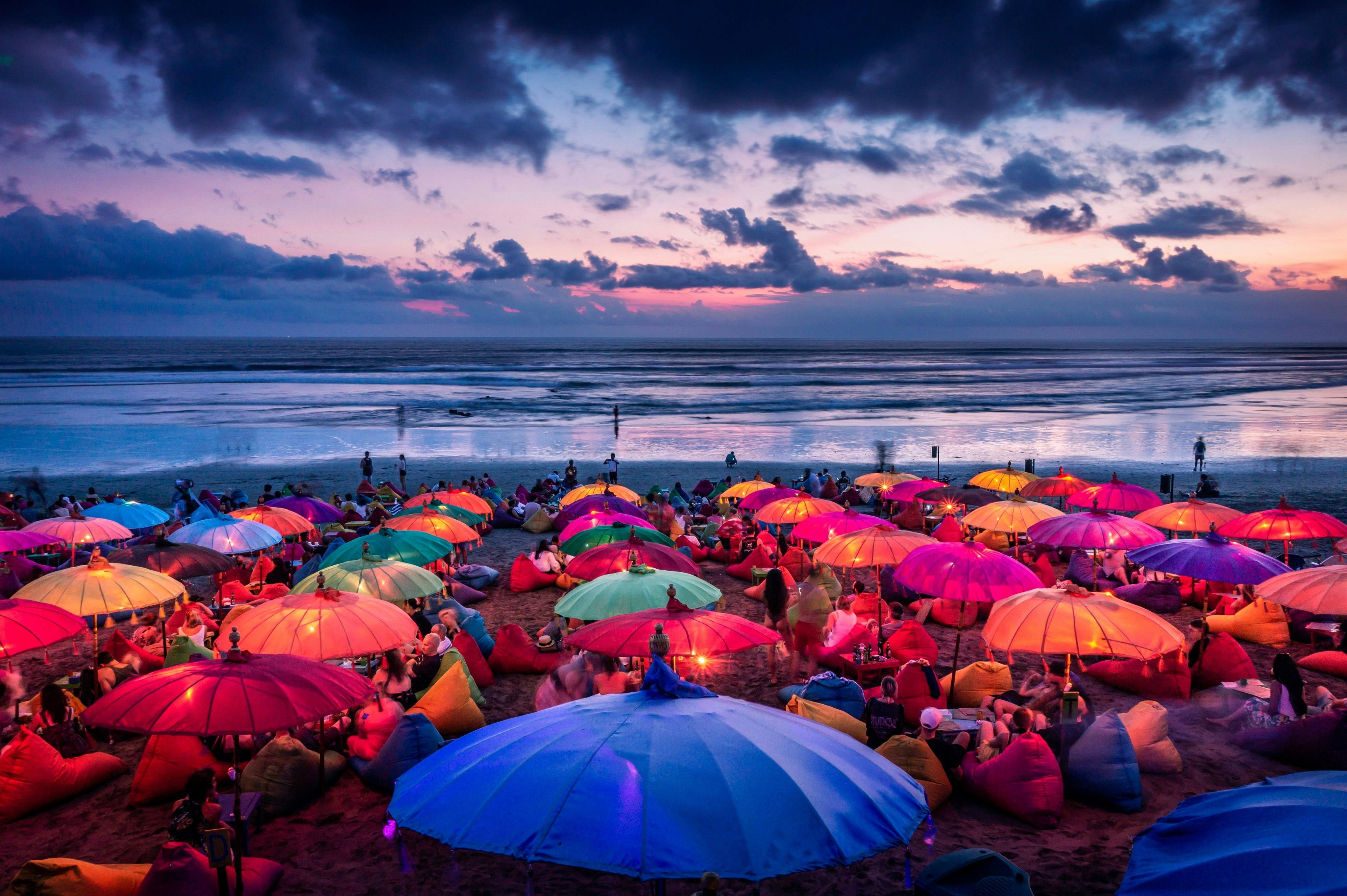 Rainbow umbrellas brighten up a beach at sunset. 