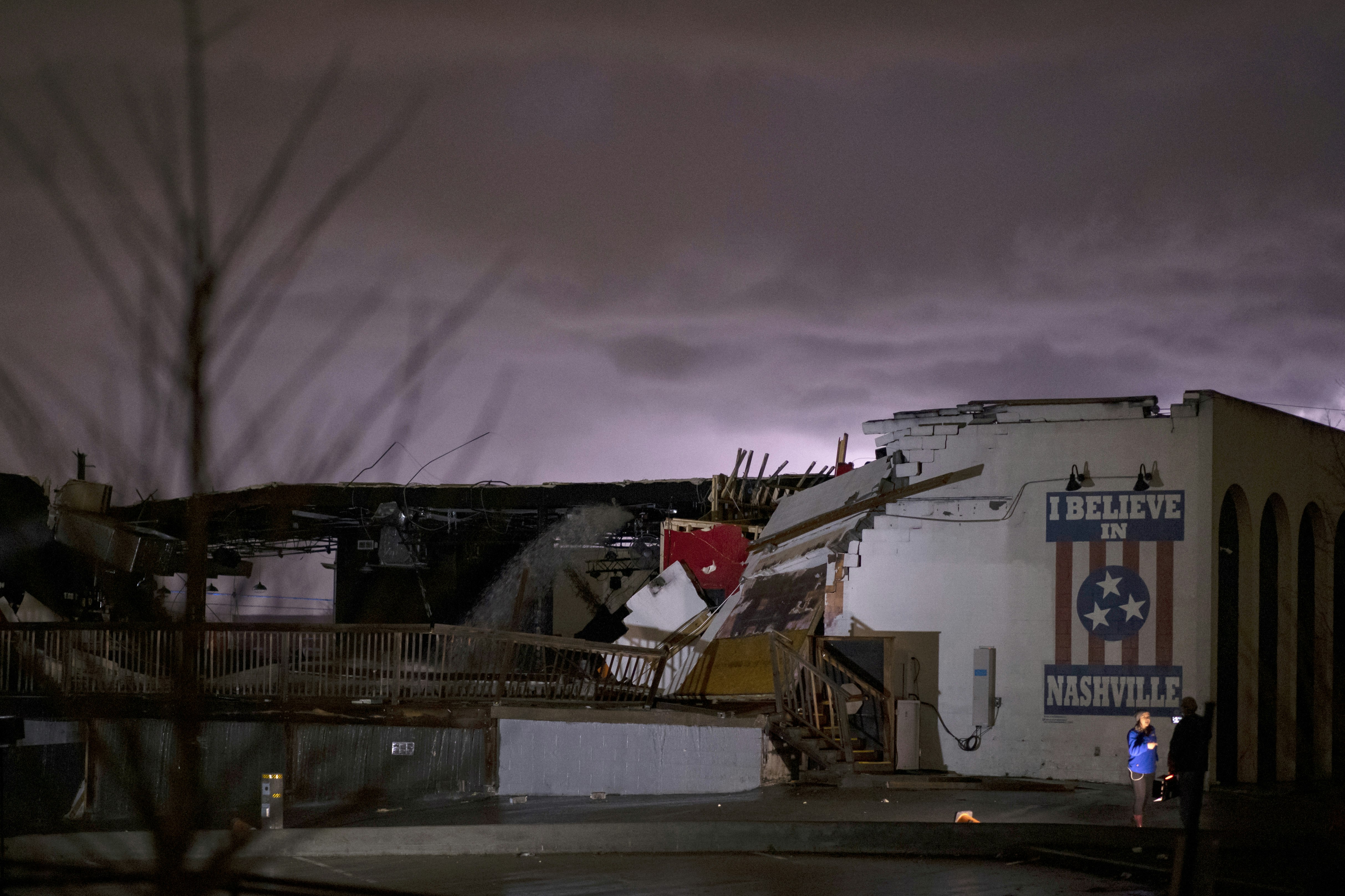 En kuslig lila himmel lyser över en vit tegelvägg med en väggmålning med texten I Believe in Nashville, en av de enda delarna av Basement East-fasaden som fortfarande står kvar efter Nashville-tornados