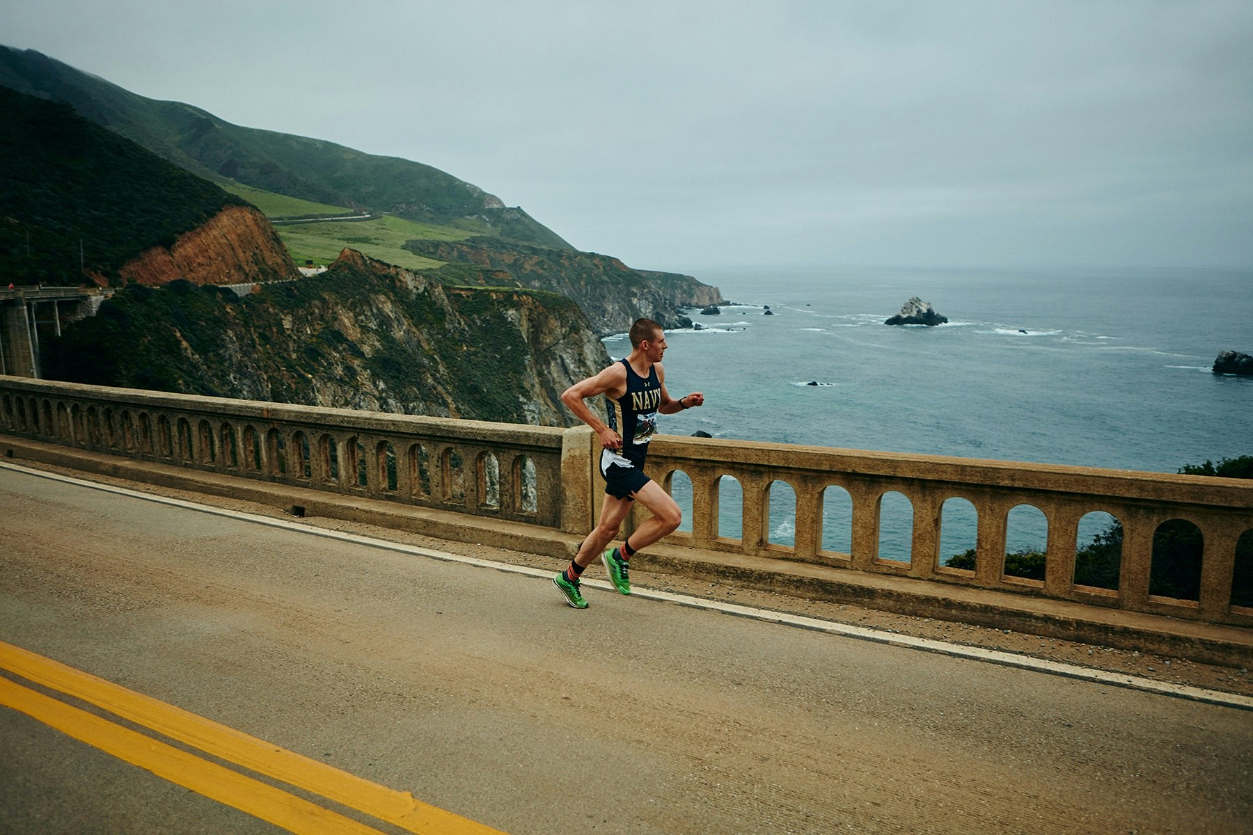 A lone runner heads along the coastal highway in the Big Sur International Marathon; beyond the stone railing the road drops off to cliffs and the Pacific Ocean