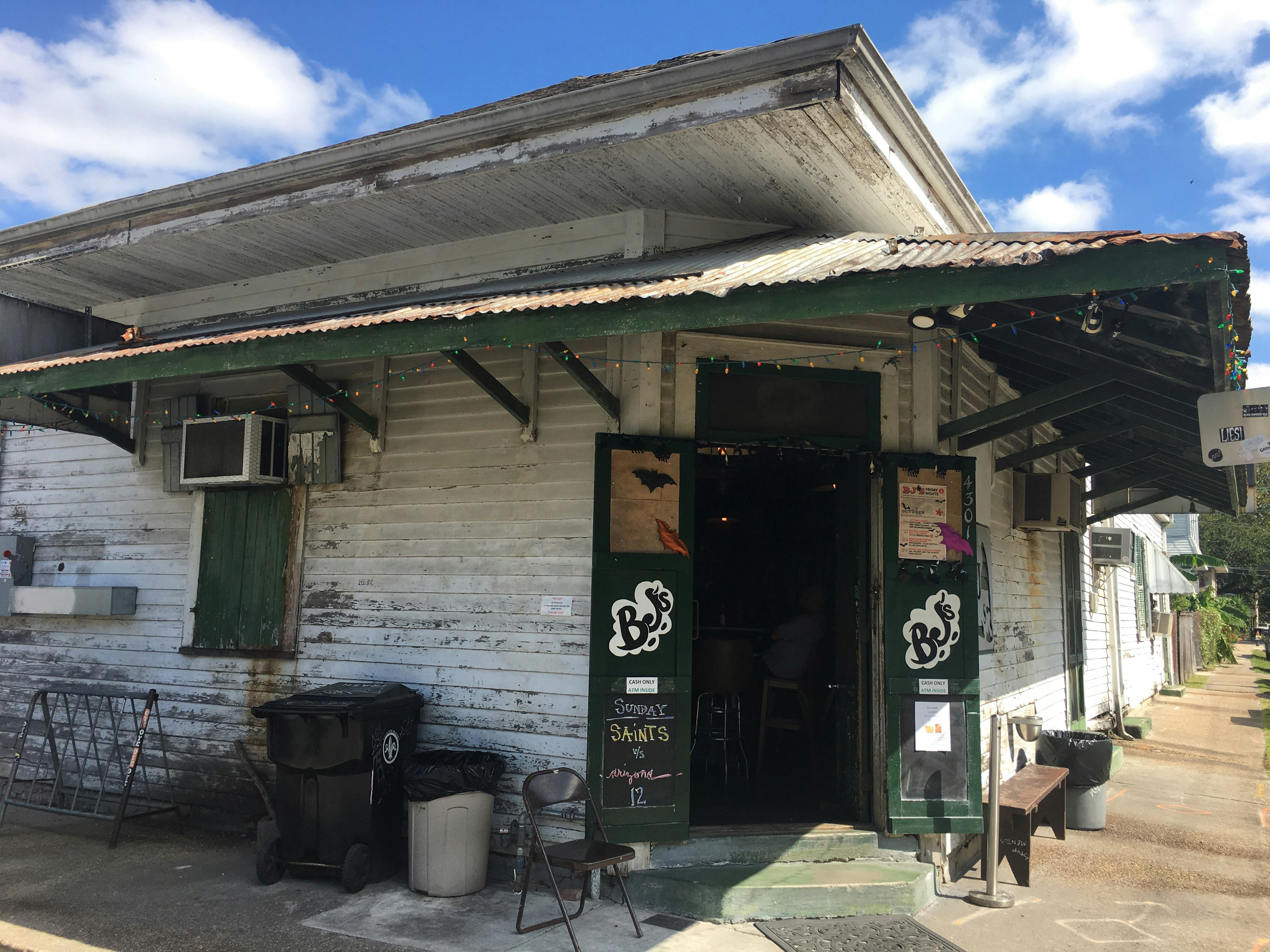 Exterior shot of Bj's bar. A pair of green doors painted with the Bj's logo are open and lead into the bar. There is a rusty awning that wraps around the bar.