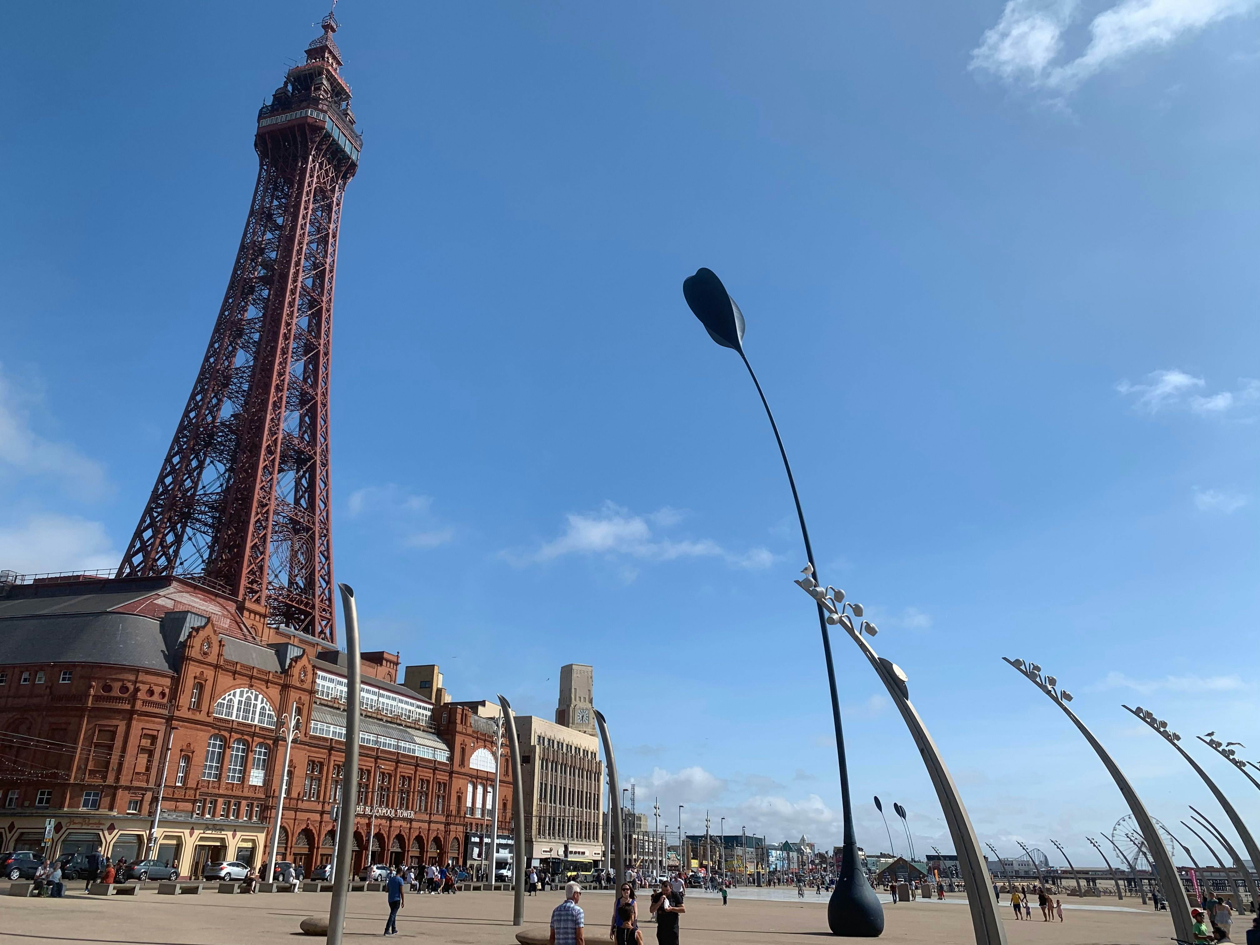 Many people walk along the Promenade by Blackpool Tower on a sunny day.