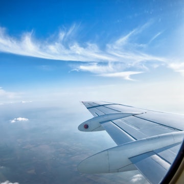 Looking through window aircraft at wing during flight with blue sky.