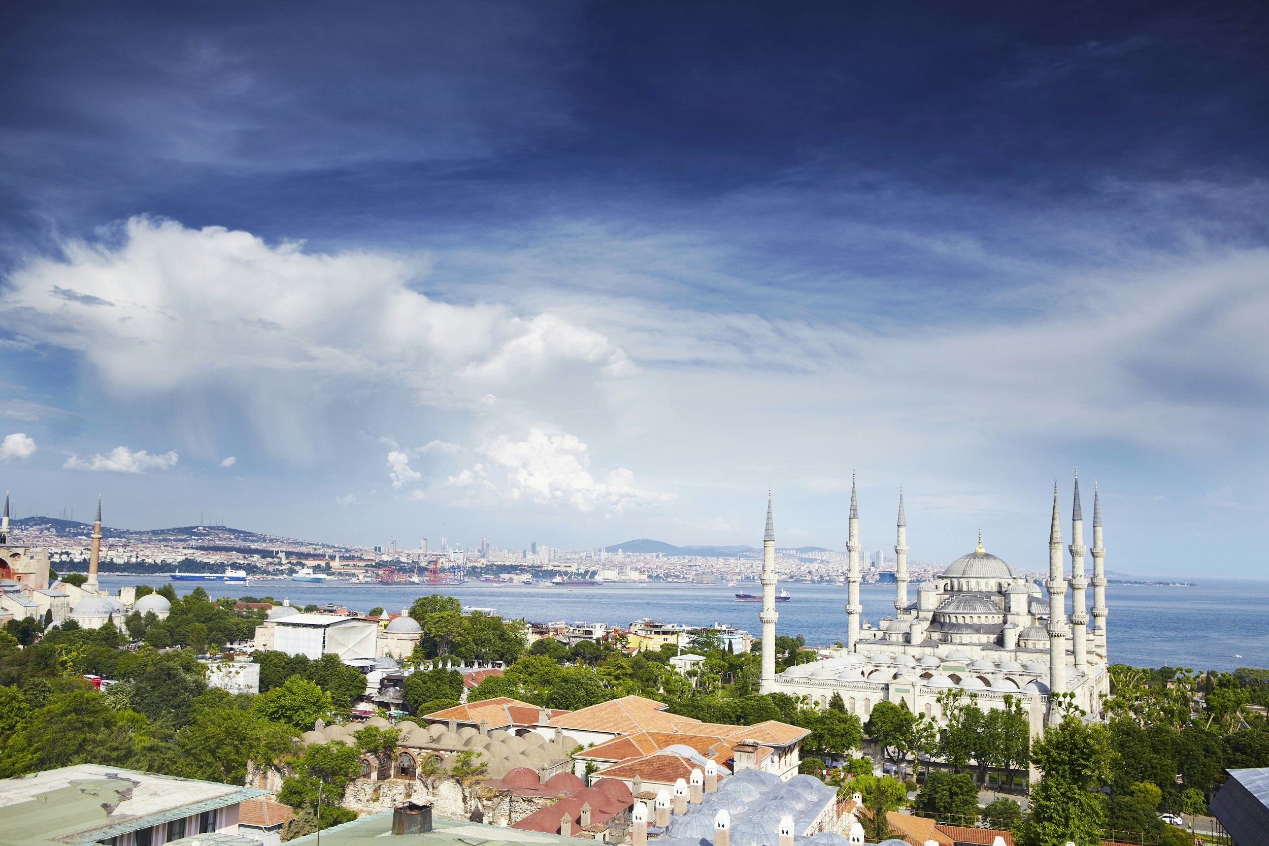 Rooftops leading to the domes and six minarets of the Blue Mosque, with the wide Bosphorus strait in the background.