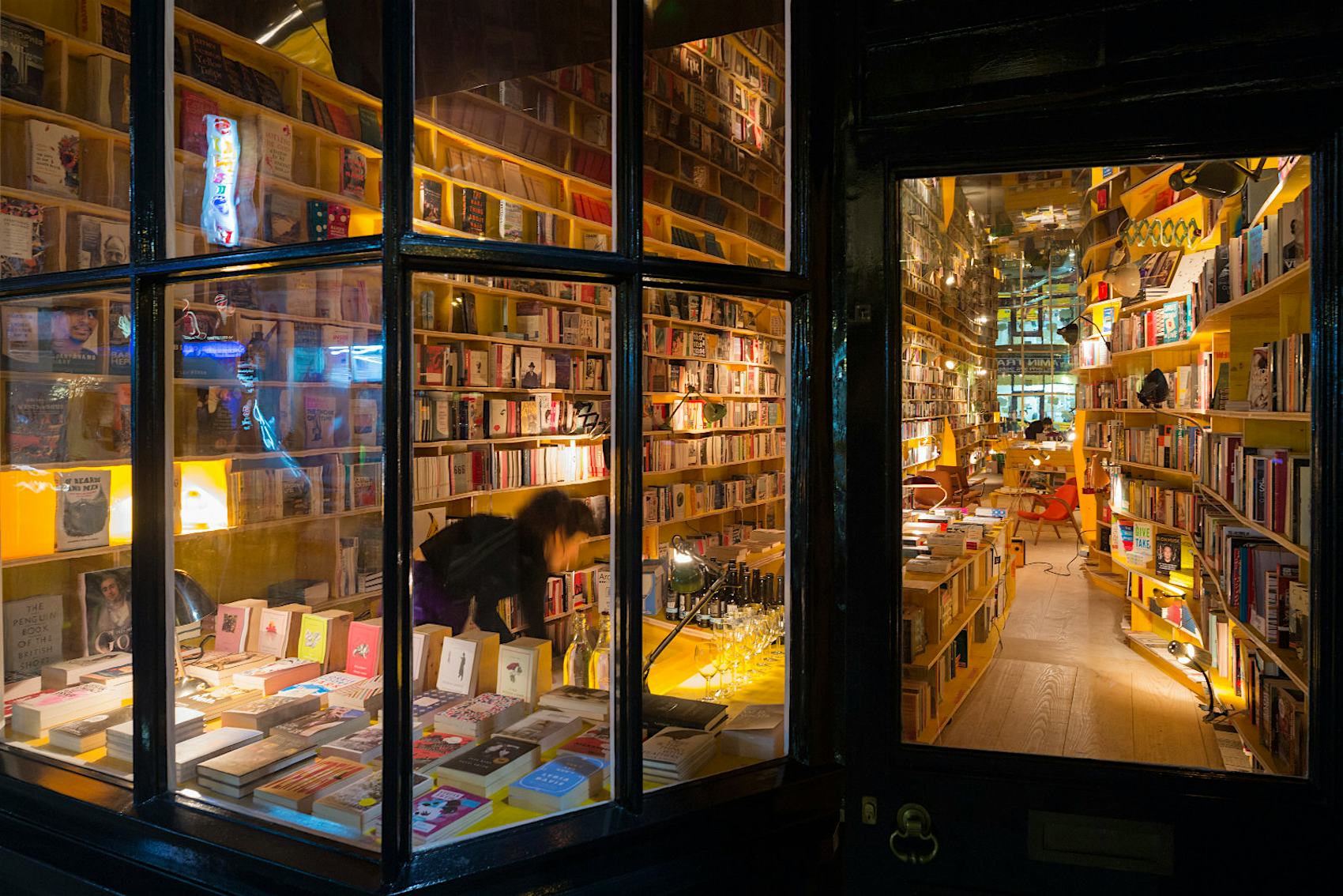Outside window of The lights of Libreria Bookshop where a person looks at books