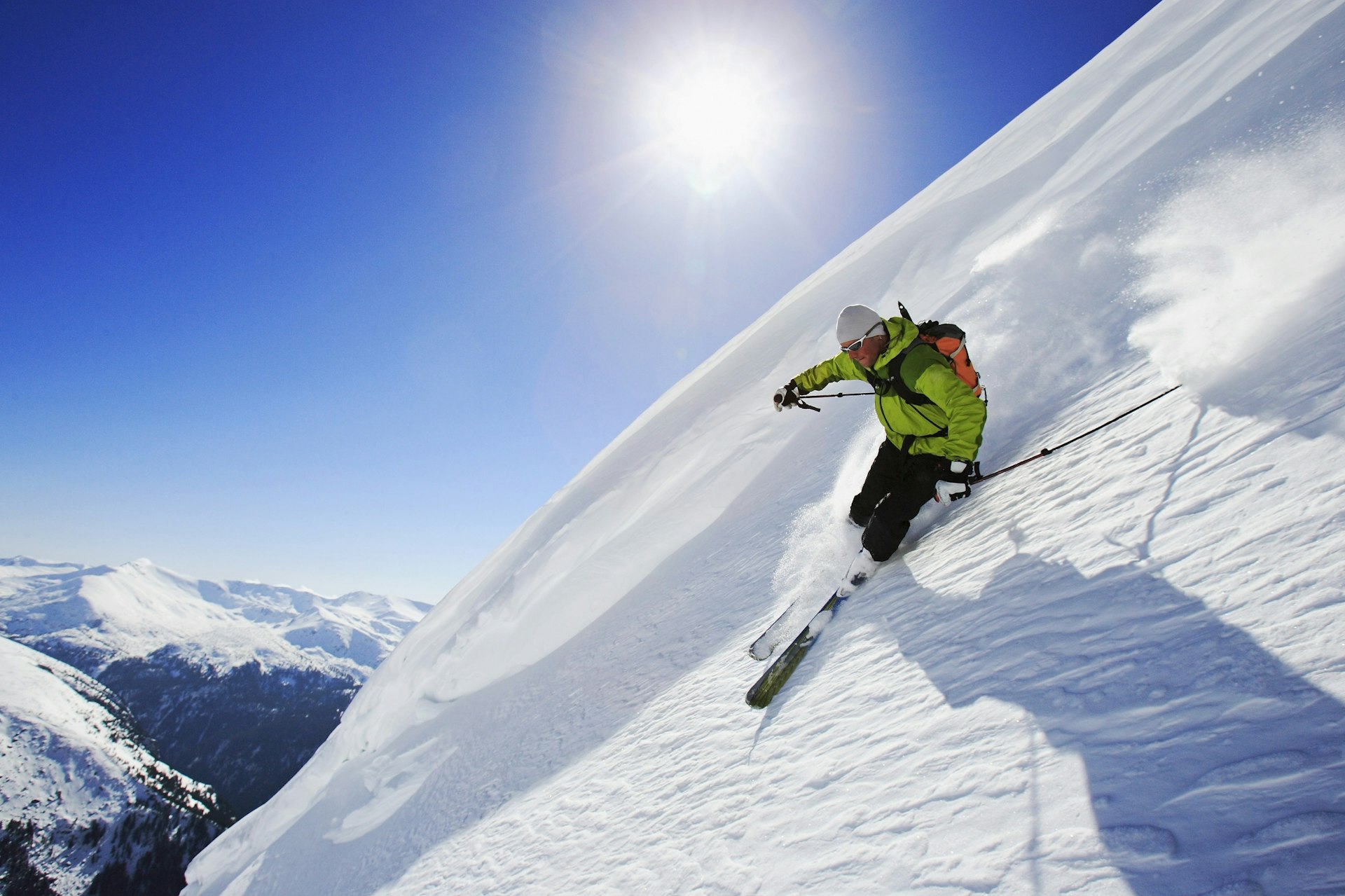 A skier makes a sharp turn on a steep slope of virgin snow; the slope cuts away to a beautiful backdrop of distant mountains.