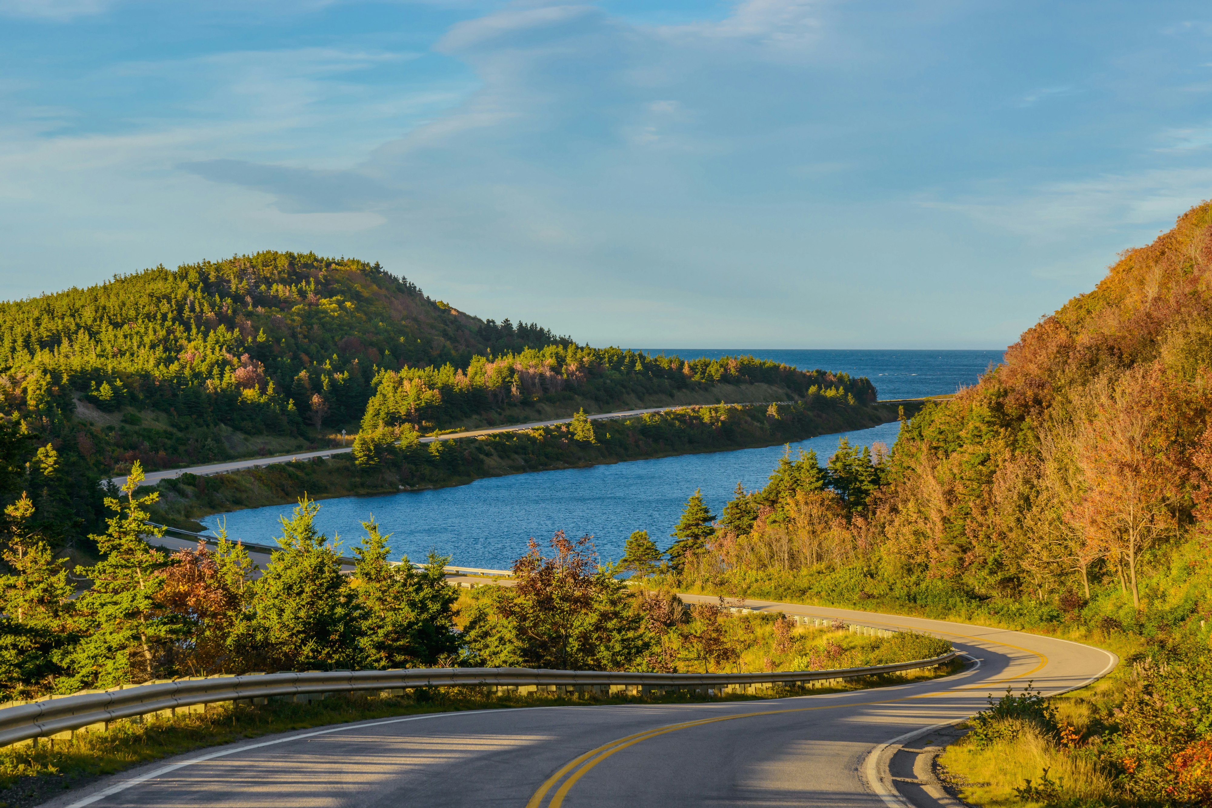 A winding coastal road on Canada's Cabot Trail; the Atlantic Ocean is on one side of the road, dense forest is on the other.