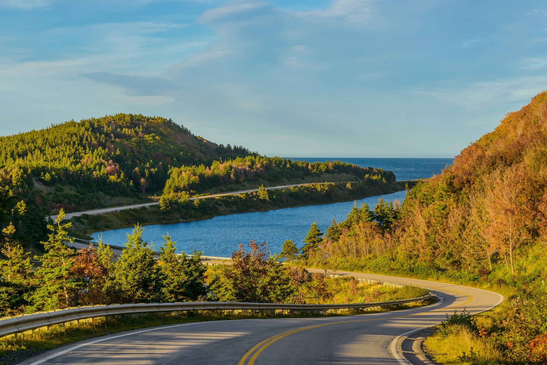 A winding coastal road on Canada's Cabot Trail; the Atlantic Ocean is on one side of the road, dense forest is on the other.