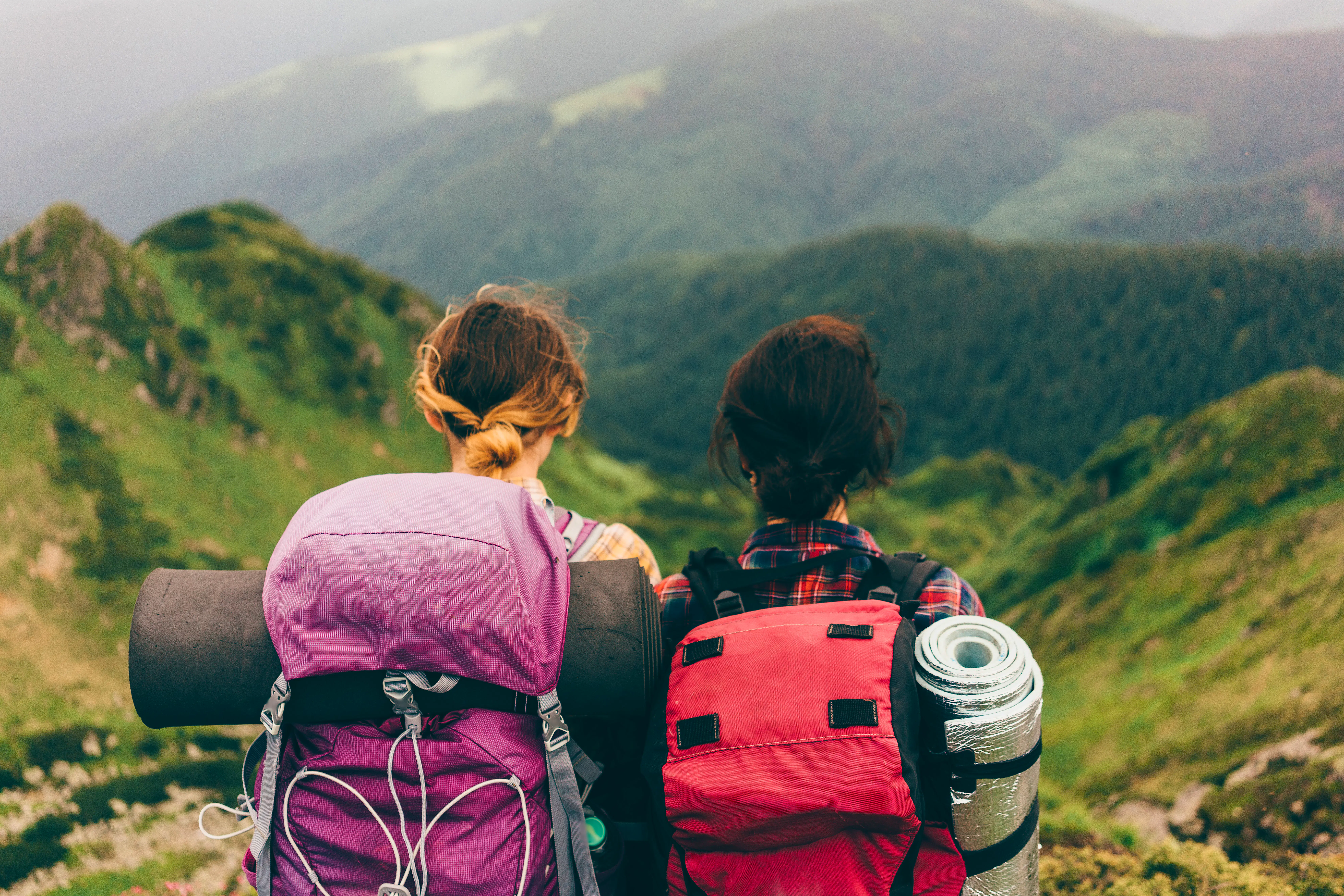 Camping in the countryside Two women stand facing rolling green hills while wearing backpacks full of camping gear.