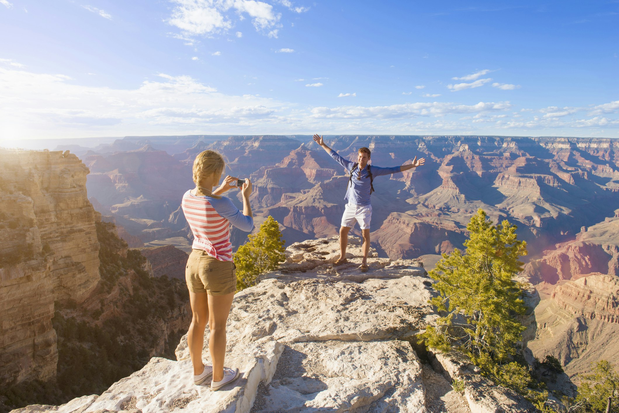 A picture of a woman snapping a picture of a man in front of a canyon