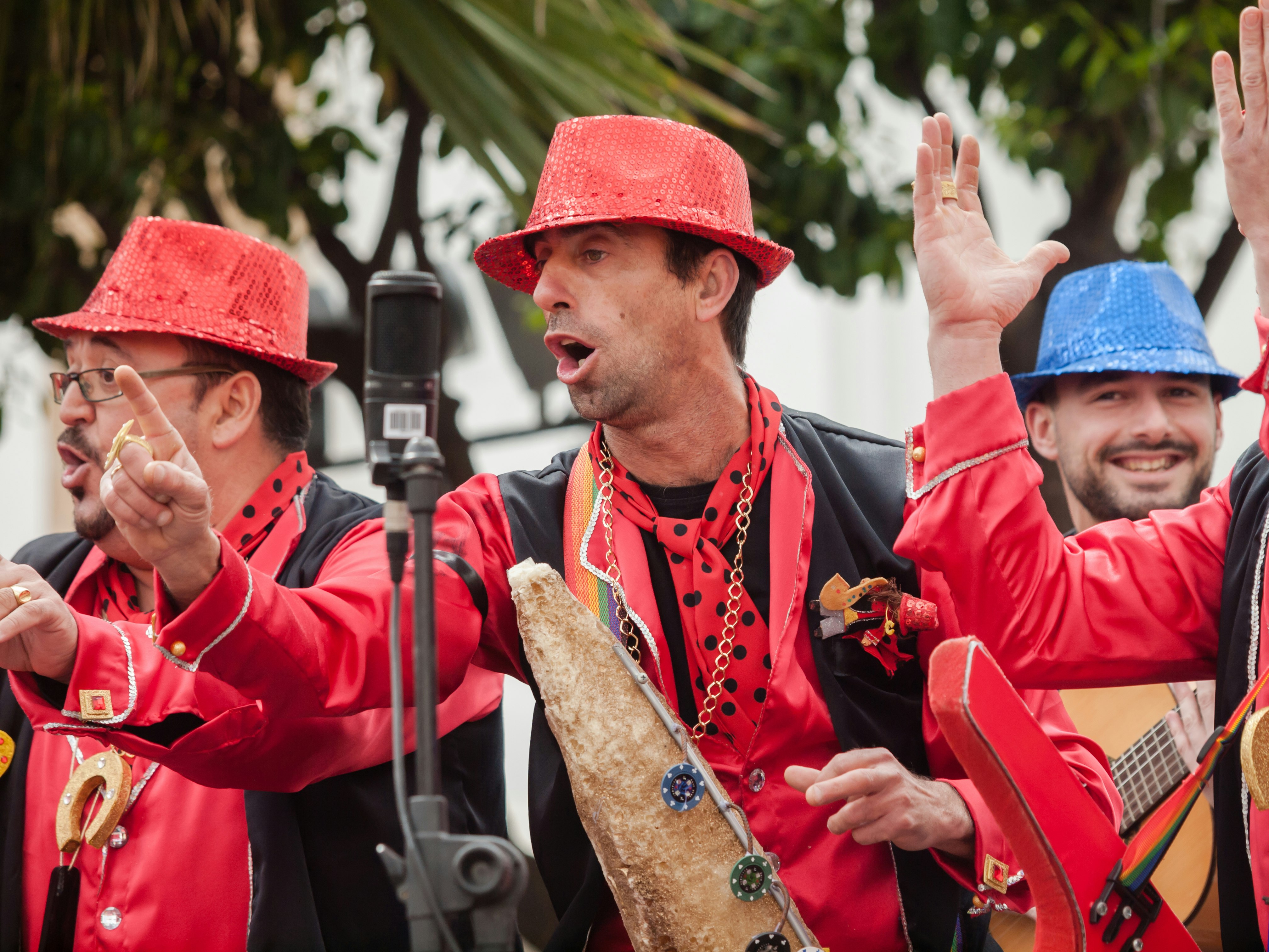 Men in red and black costumes stand around a microphone singing at Cádiz Carnival, Spain.
