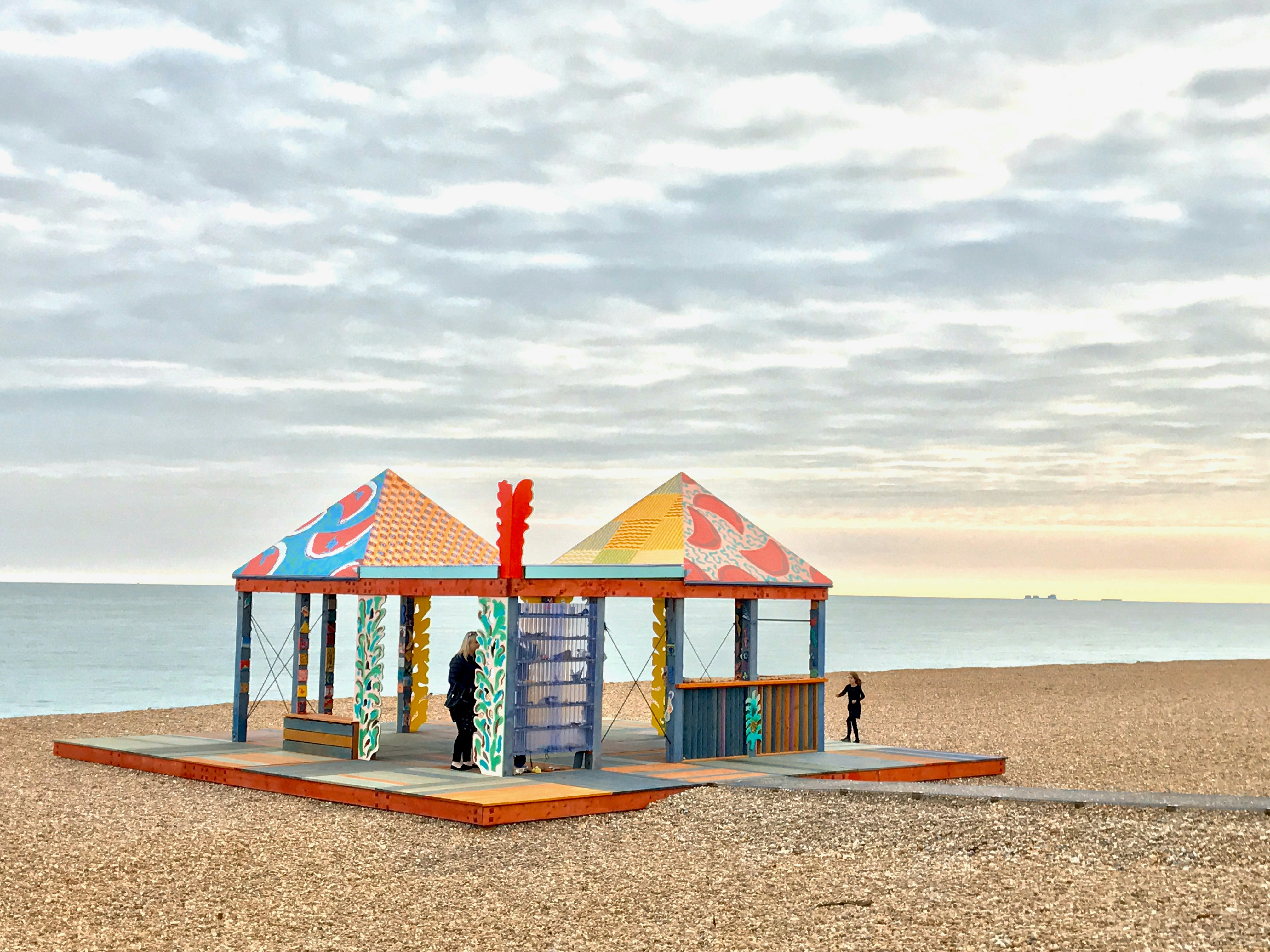 Two brightly painted pagodas, and artwork by Sol Calero for the 2017 Folkestone Triennial, stand on a platform on Folkestone's pebbled beach.