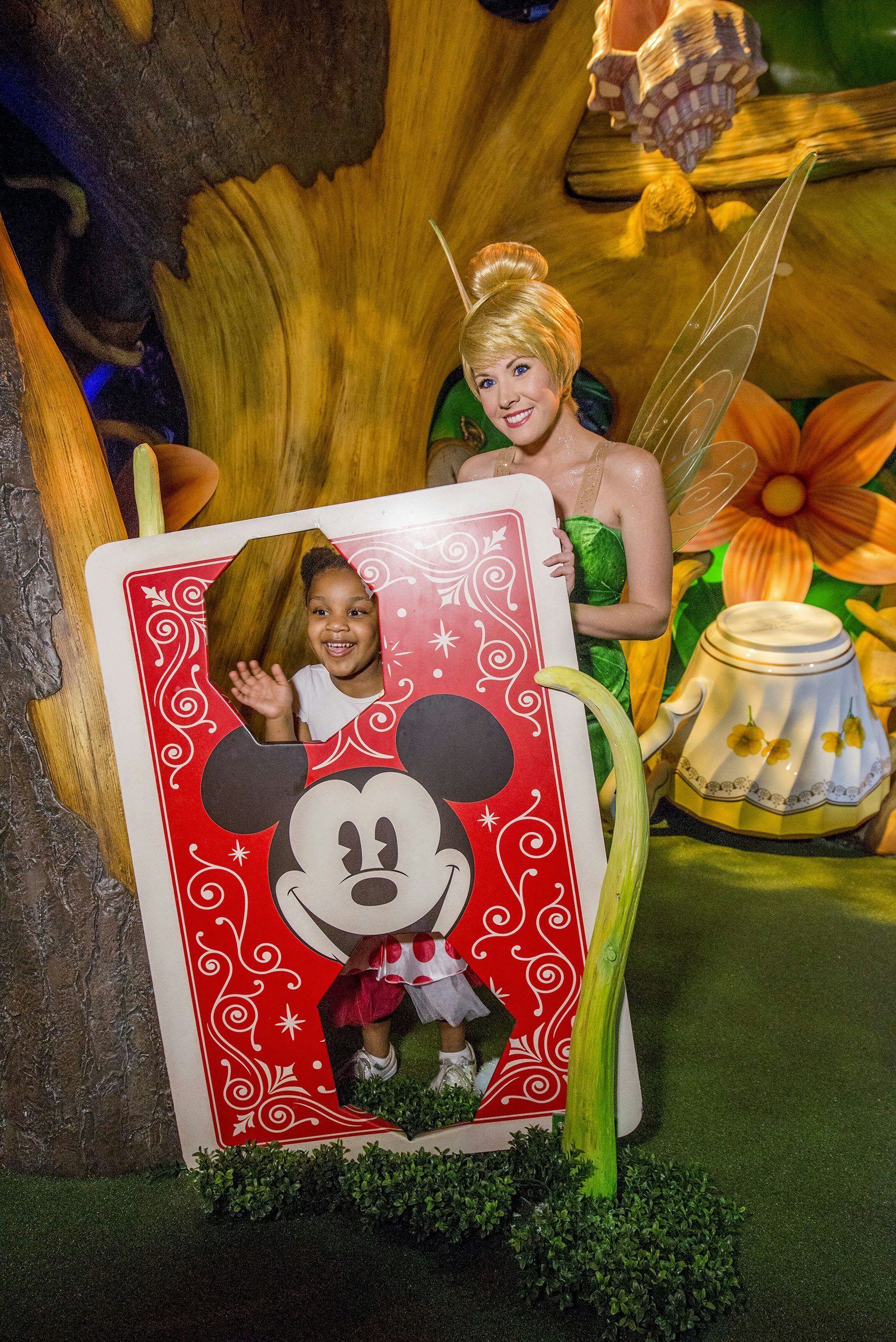 Tinker Bell strikes a pose with a young girl behind a large Mickey Mouse playing card
