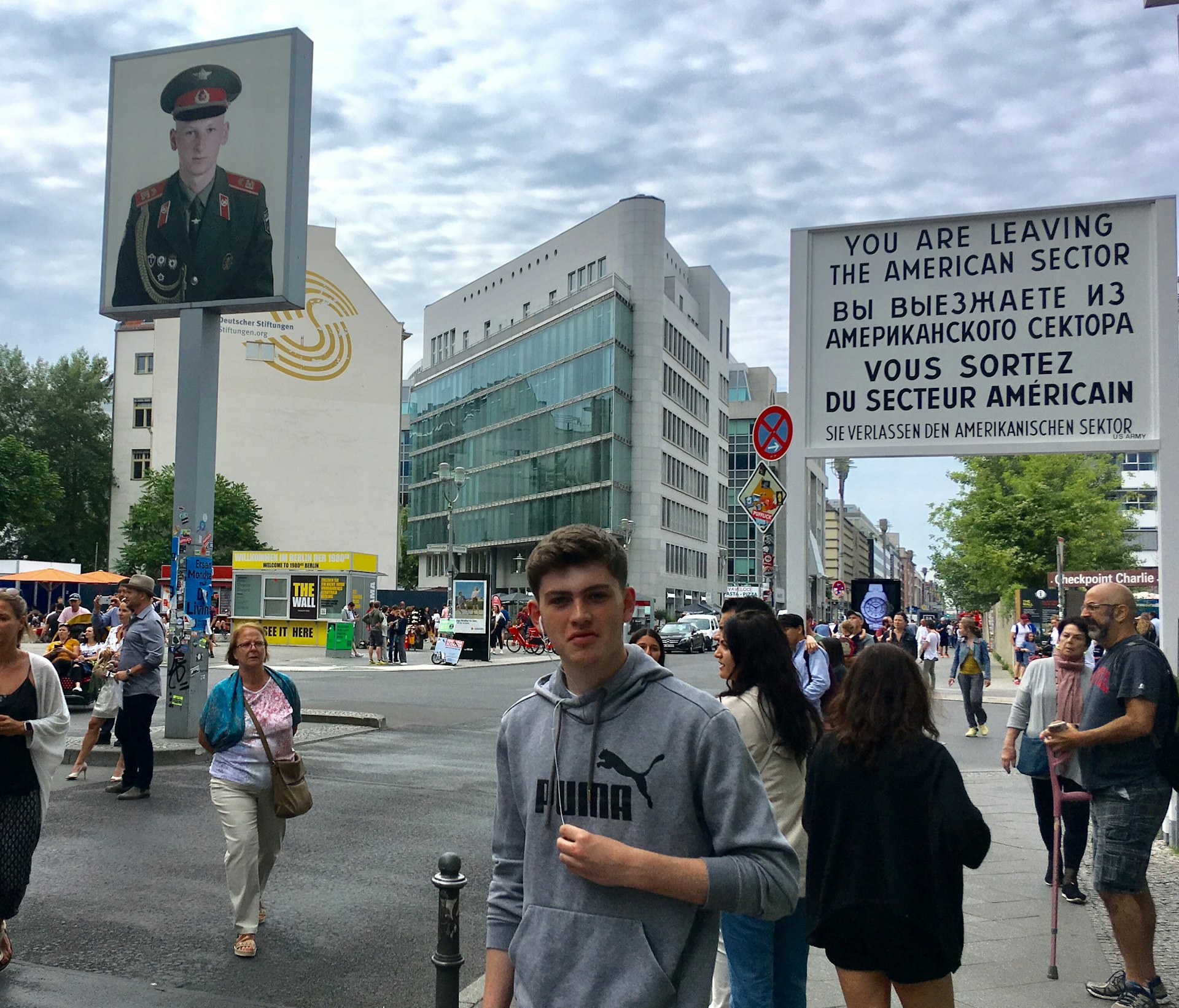 A teenage boy stands with many other people who are assembled at Berlin's Checkpoint Charlie.