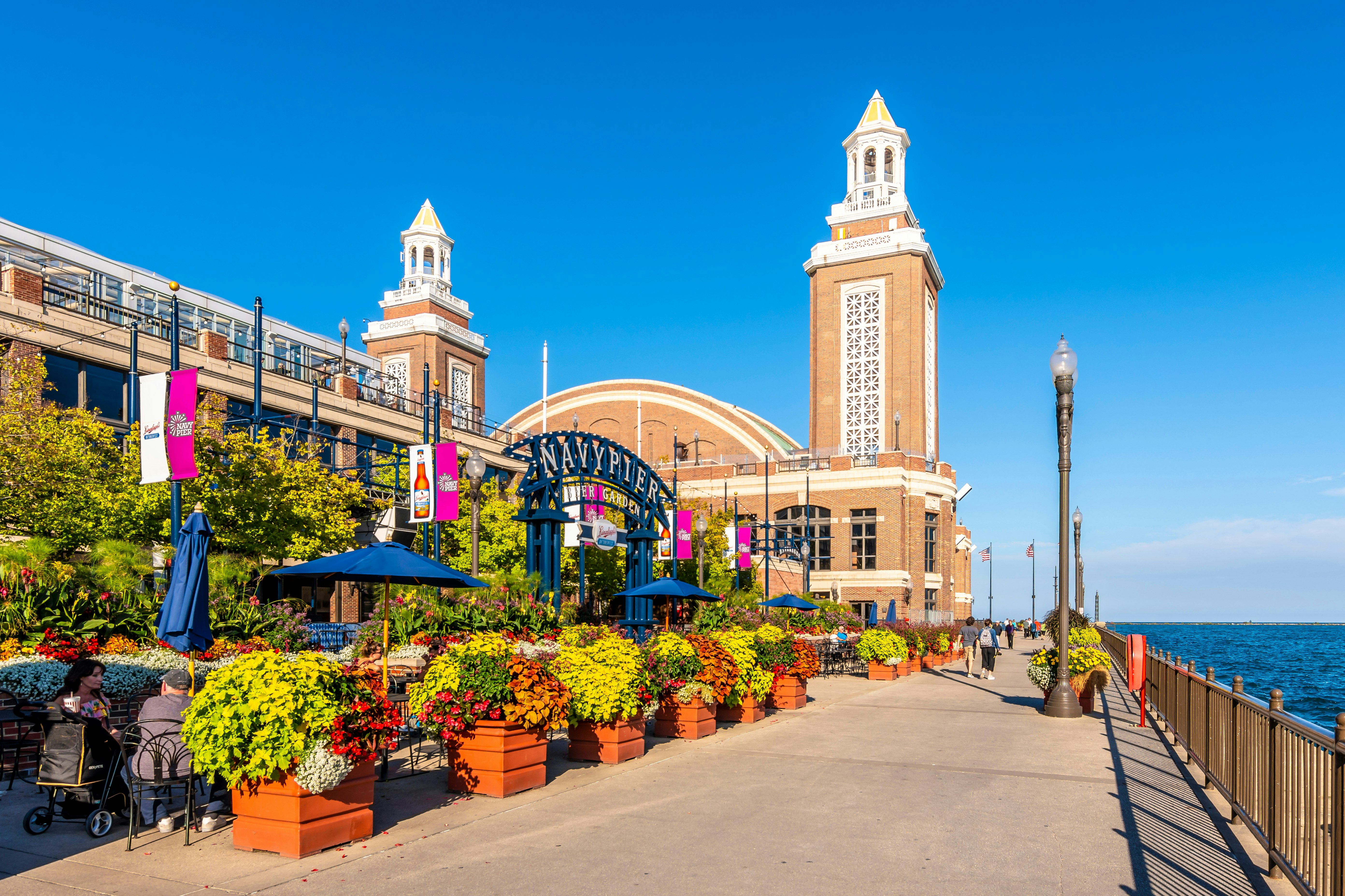 A red-brick building with two towers at the end of pier; the exterior is decorated with potted plants and trees.