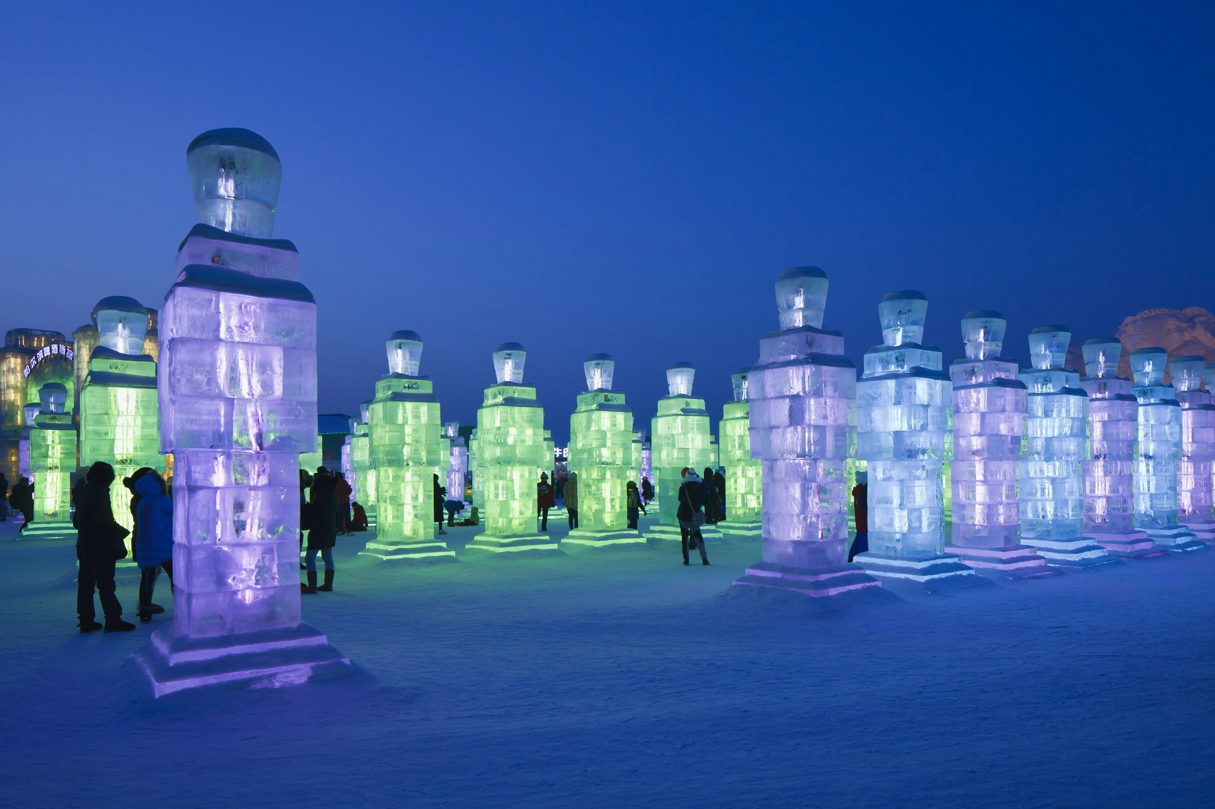 People chad in warm winter clothing mill around huge 6m-tall ice-block statues that are glowing purple, blue or green.