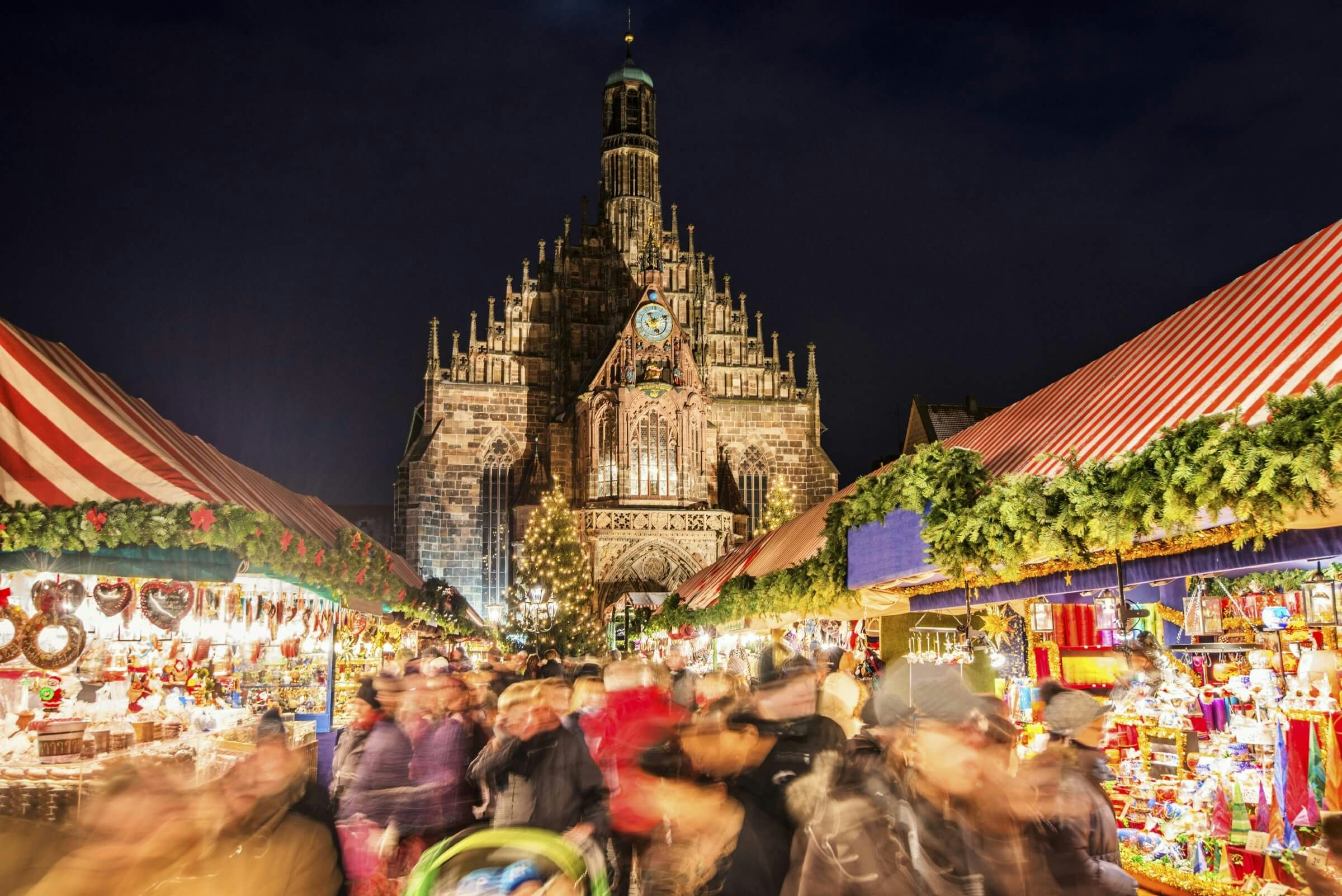A blurred image of peoples and stalls and lights at a Christmas market with the Frauenkirche church in sharp focus in the background