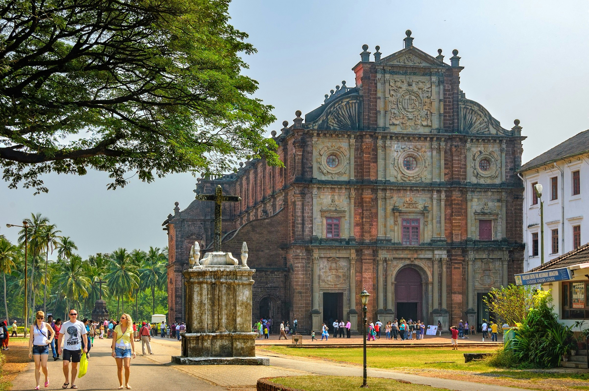 An imposing Portuguese church located in Old Goa, looming over the surrounding palm trees and scattering of people walking around the grounds.