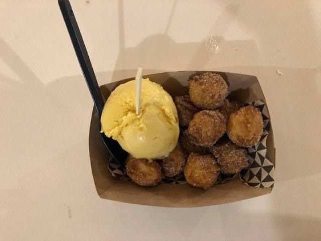 A cardboard dish filled with spherical churros, and a scoop of ice cream.