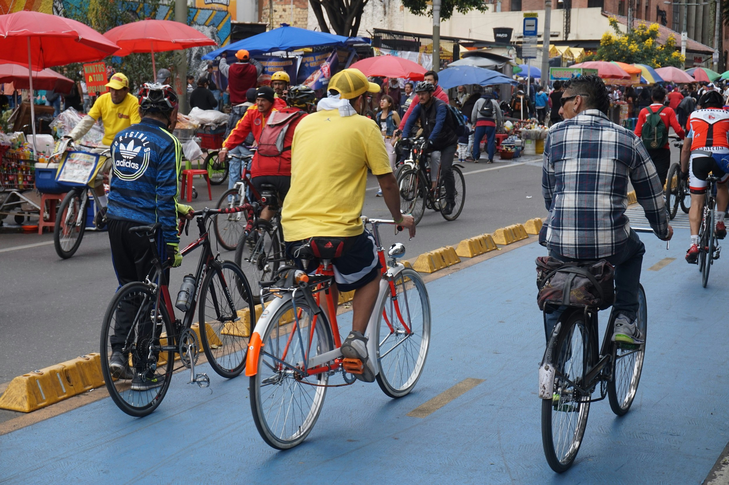 A street is filled with people on bicycles riding both directions; on the side of the street that is visible there are numerous vendors selling food.