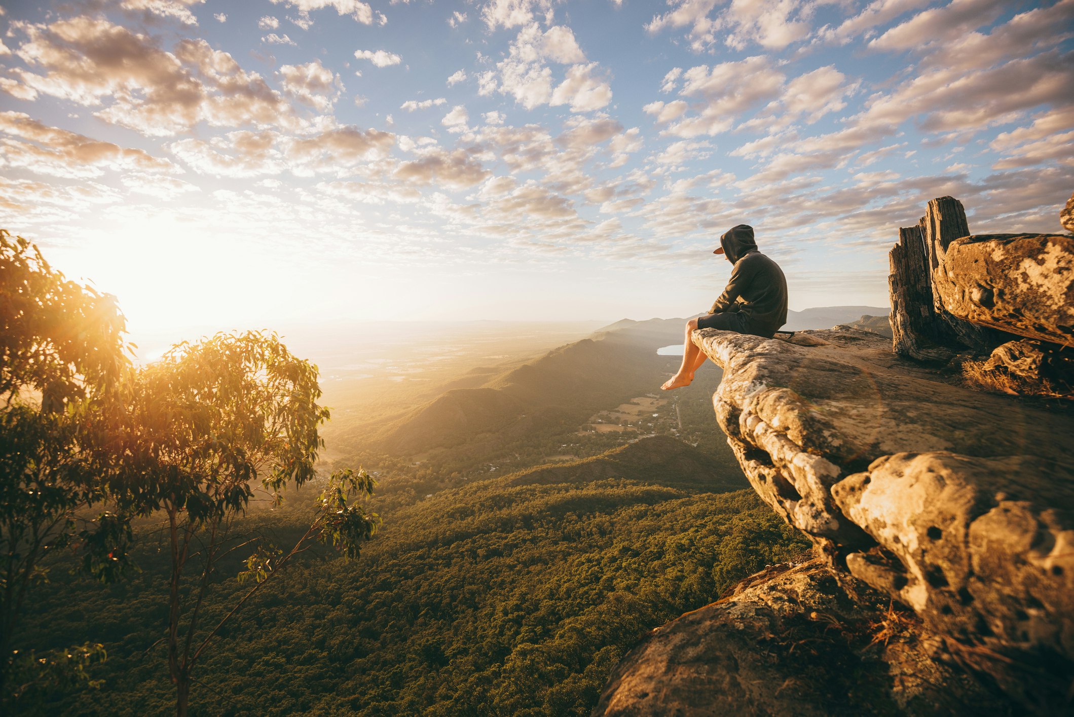 A picture of a man sitting on the edge of a cliff at sunrise
