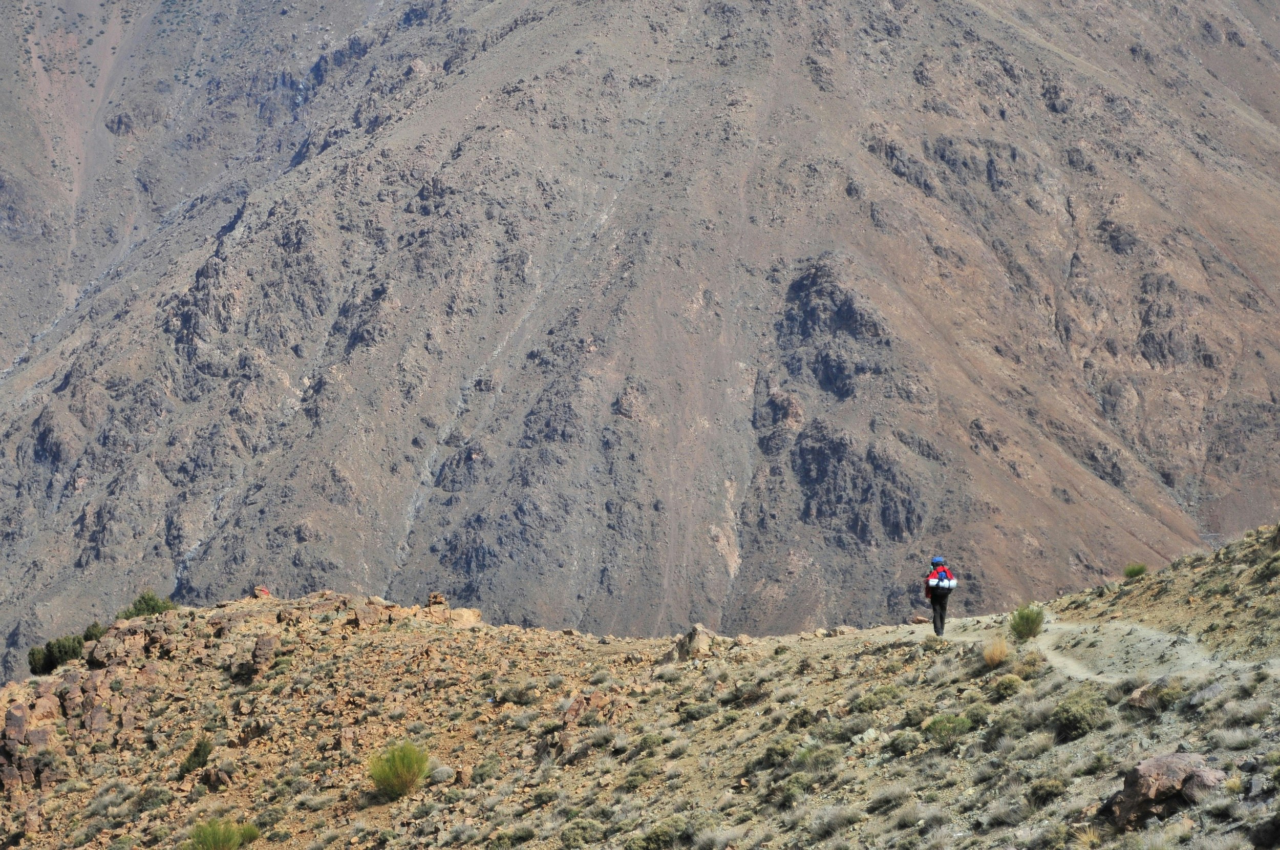 A lone hiker on a ridge who is dwarfed by the hulking mass of Jebel Toubkal in the background.