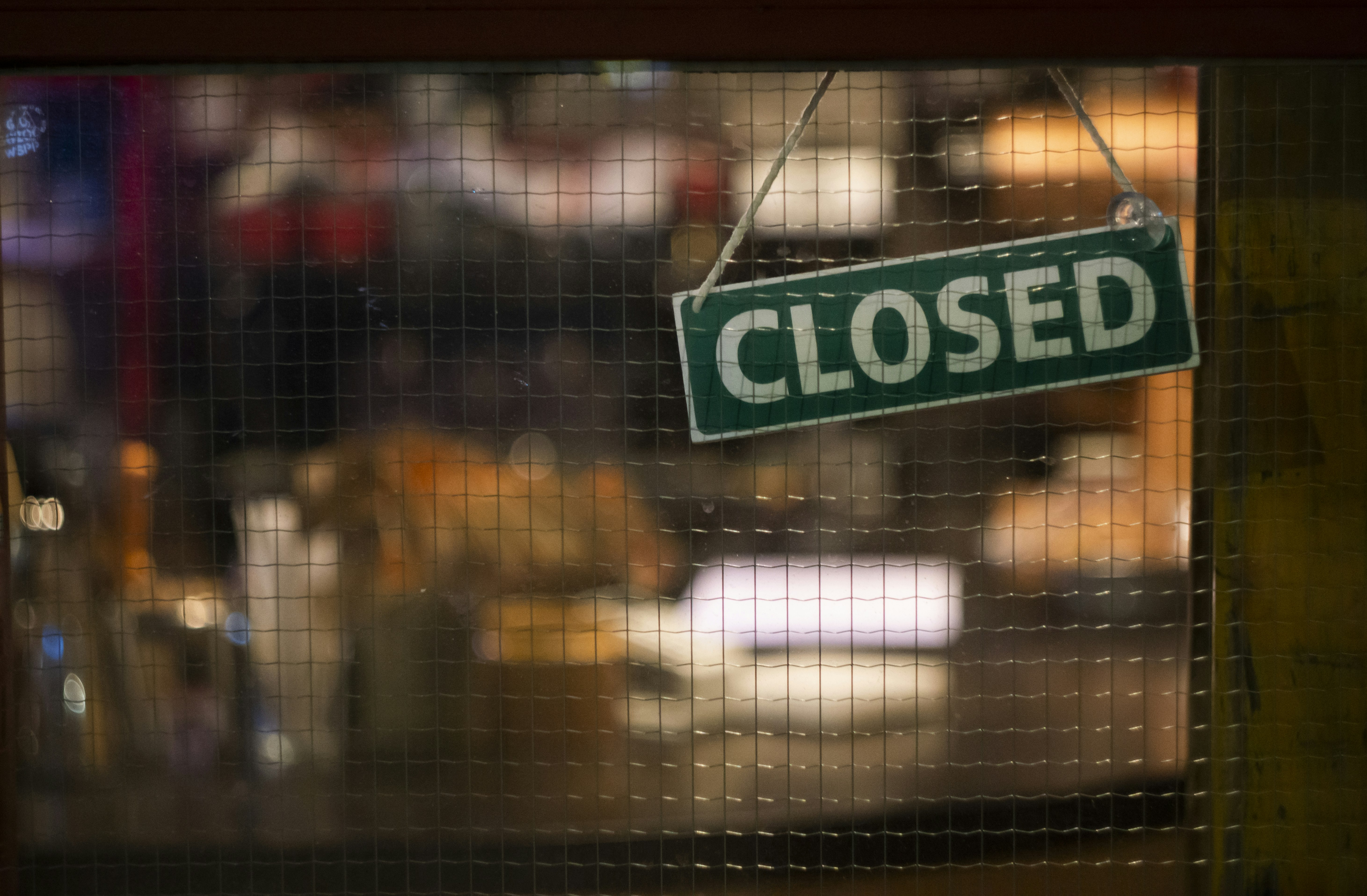 A "closed" sign in a window covered with wire