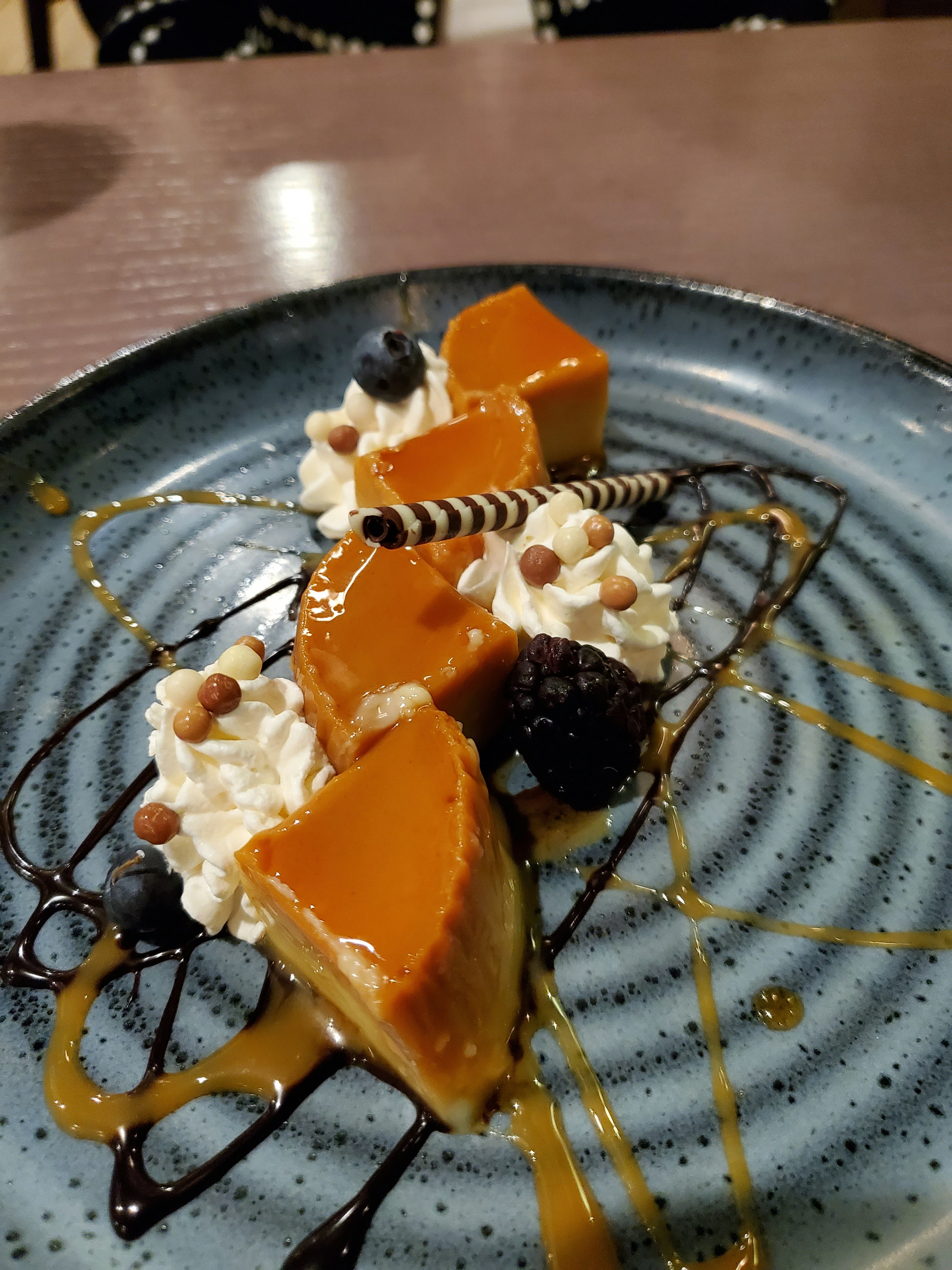 A plate of coconut flan sits on drizzles of caramel and chocolate sauce and whipped cream