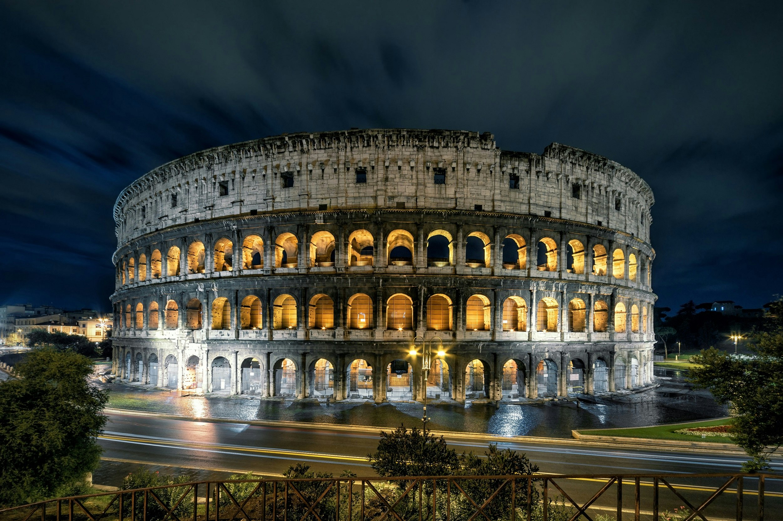 A nighttime shot of the Colosseum, which is a large, multi-storey round building with many arches. Each arch is lit up.