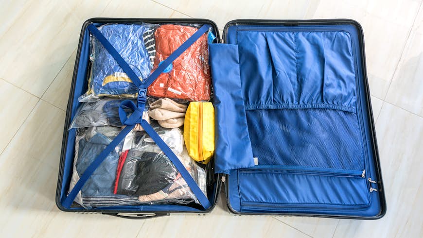 A carry-on suitcase with blue lining packed with clothes in plastic vaccum-packed sacks