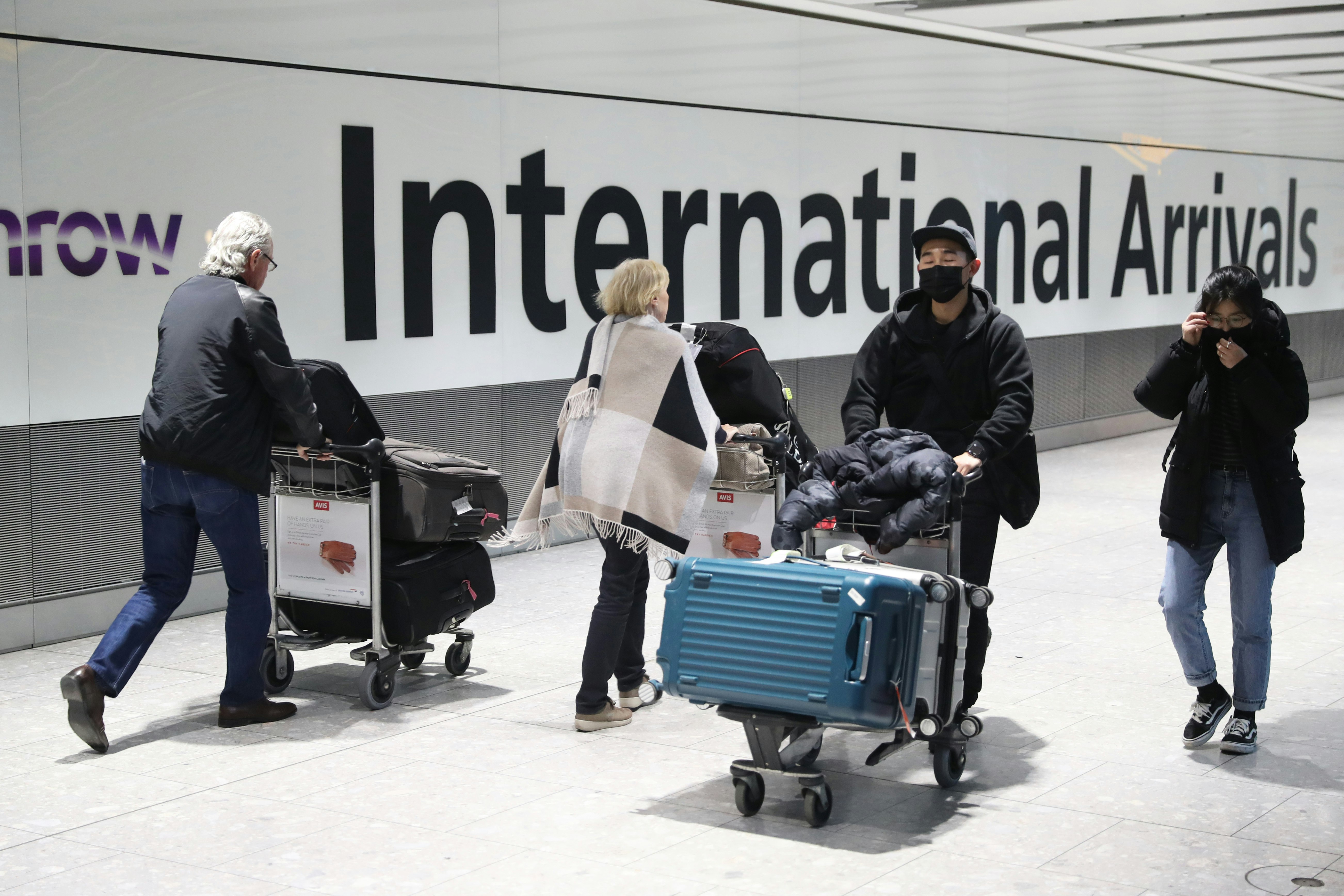 Passengers arrive in London in front of a sign that says international arrivals. 
