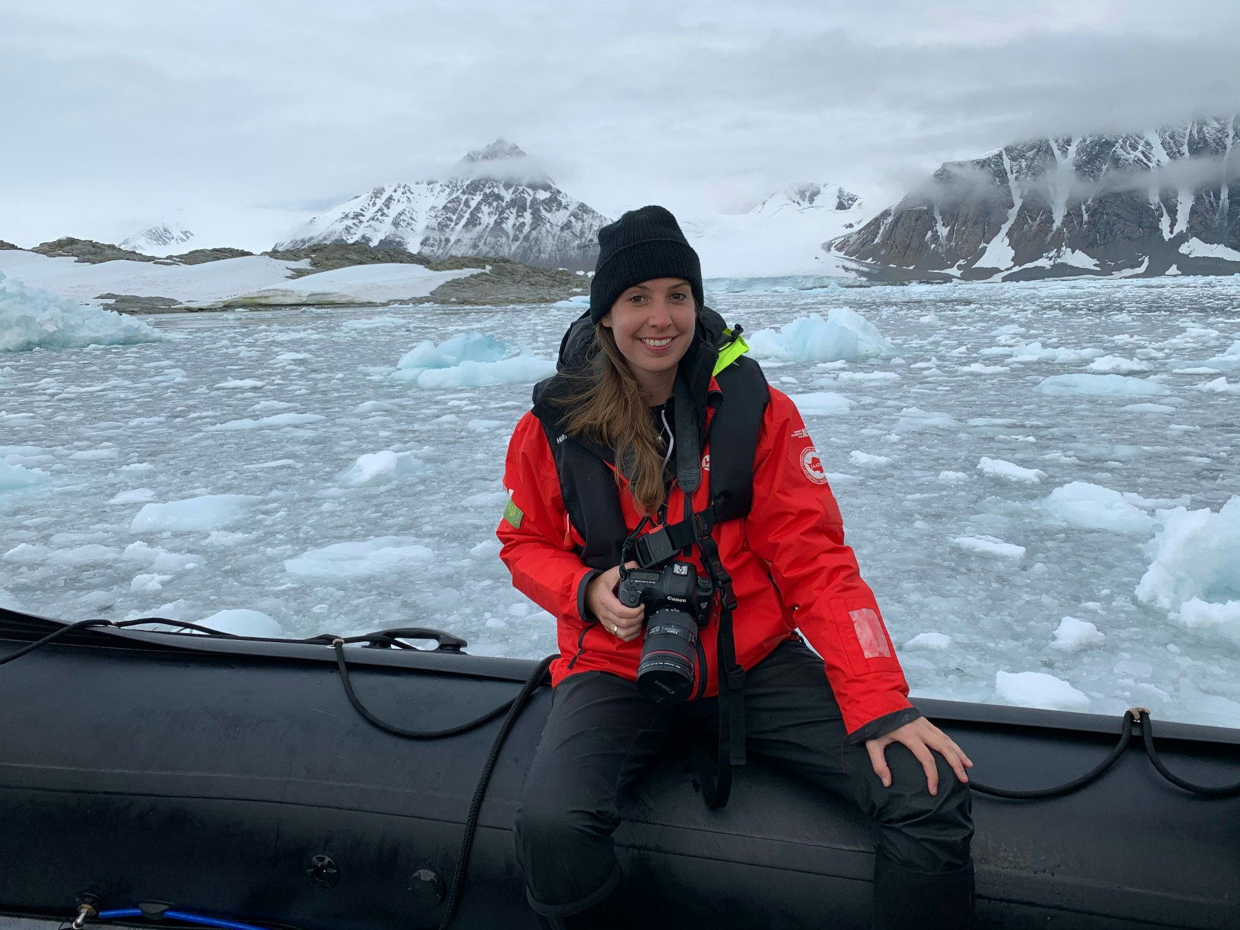 The author sits on the edge of a boat, camera around her neck, with icebergs in the back,