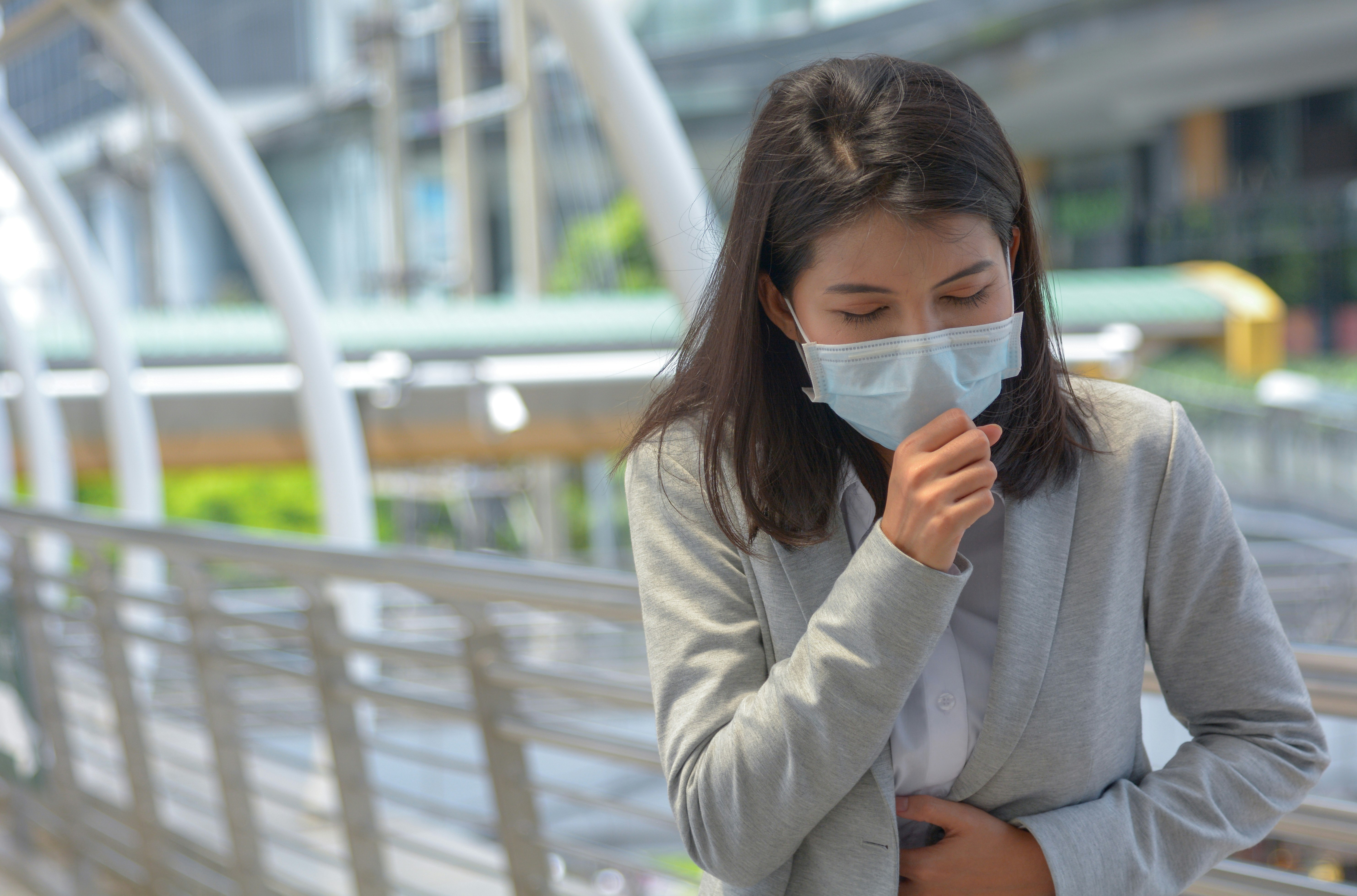 Woman coughing with a surgical mask in an airport