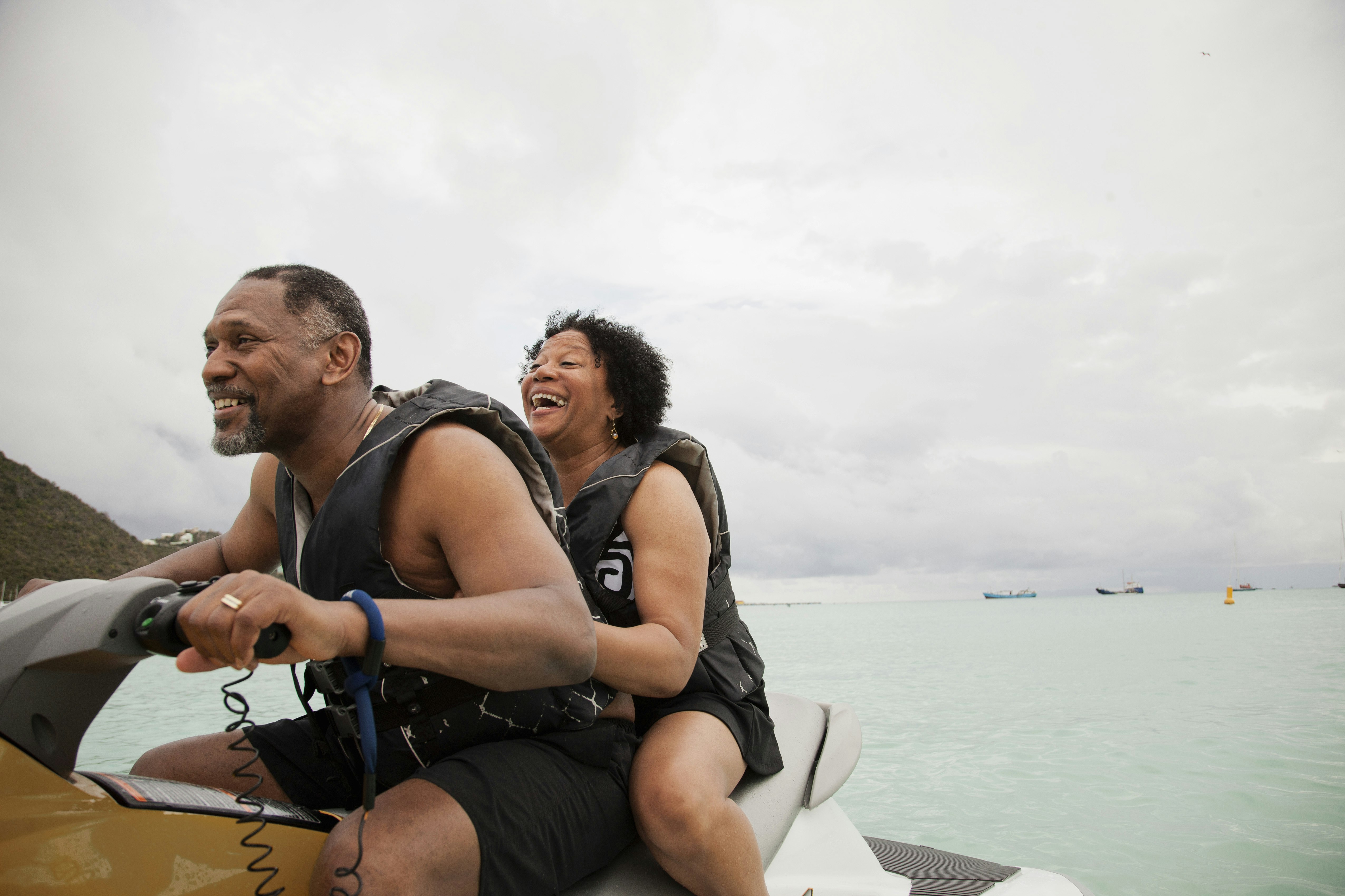 A woman smiles joyfully as she holds onto her partner, who is driving the jetski they're both riding.